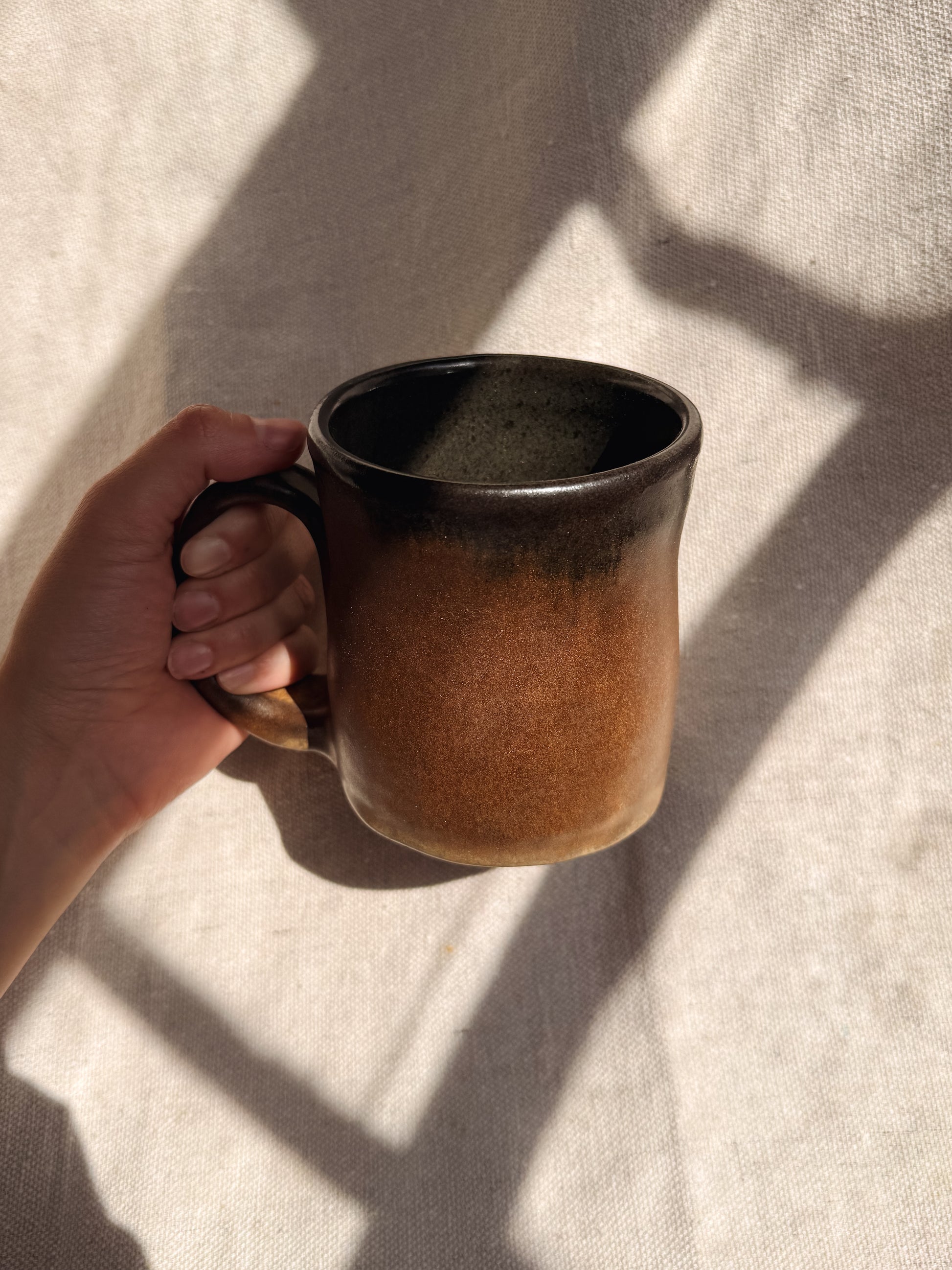 Hand holding a brown ceramic mug on a light fabric background