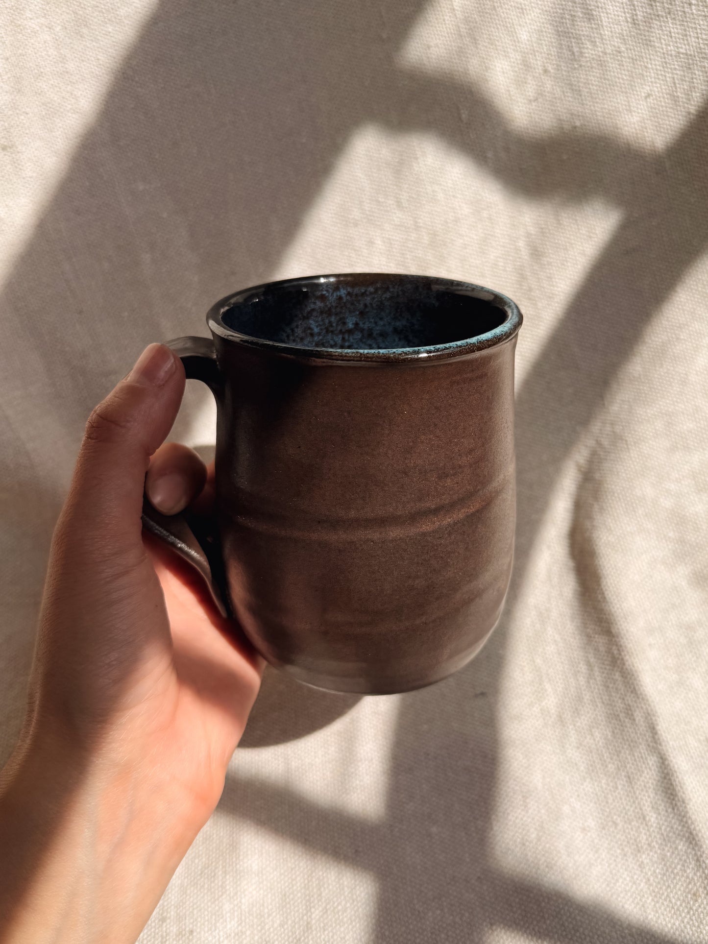 Hand holding a brown ceramic mug against a neutral background