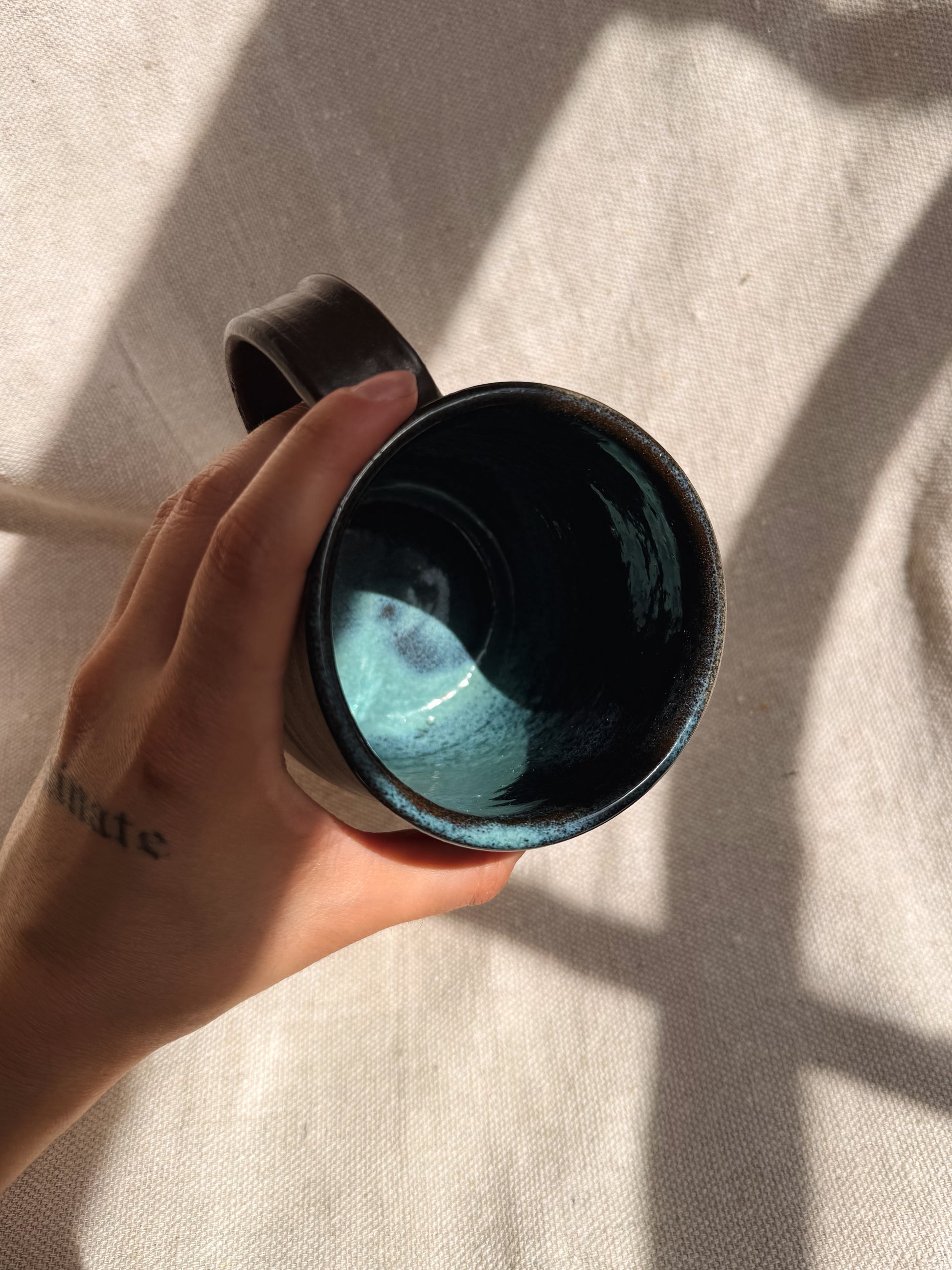Hand holding a ceramic mug with a blue interior against a neutral background
