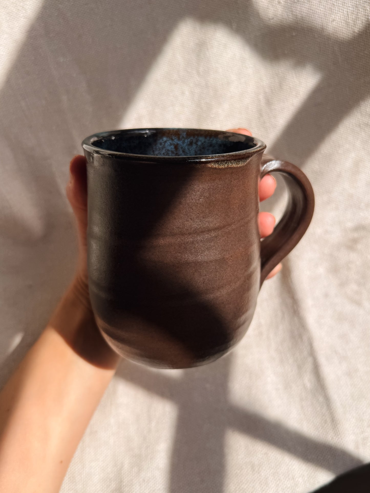 Brown ceramic mug held against a light background