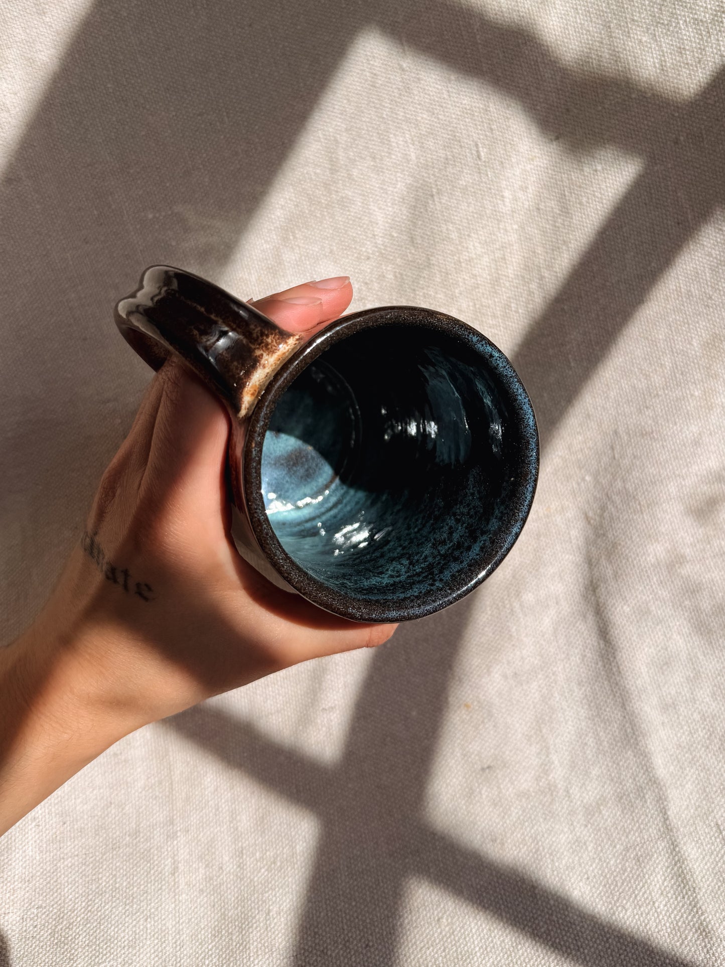 Hand holding a dark ceramic mug against a neutral background
