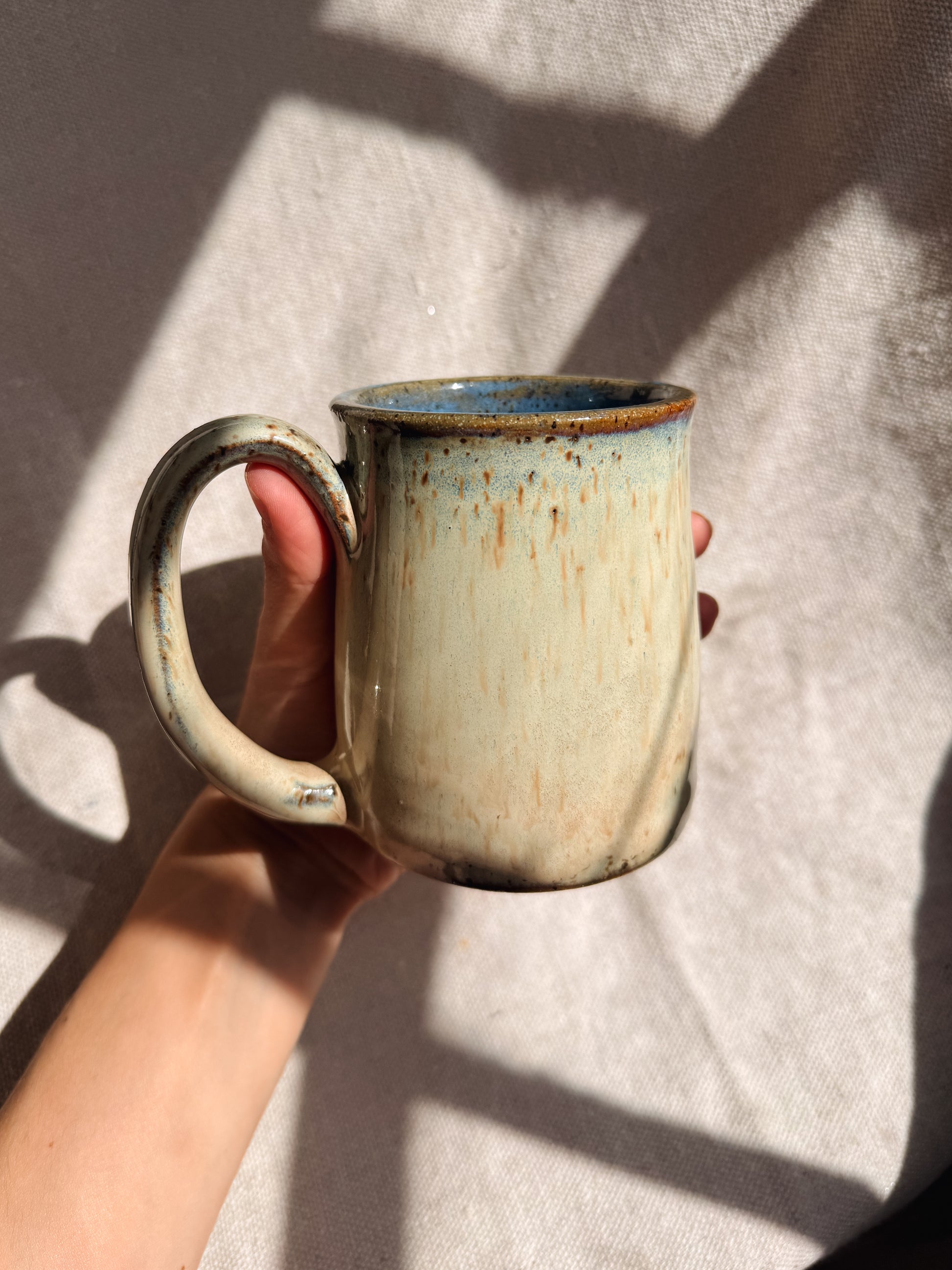 Hand holding a ceramic mug with a textured surface on a light fabric background