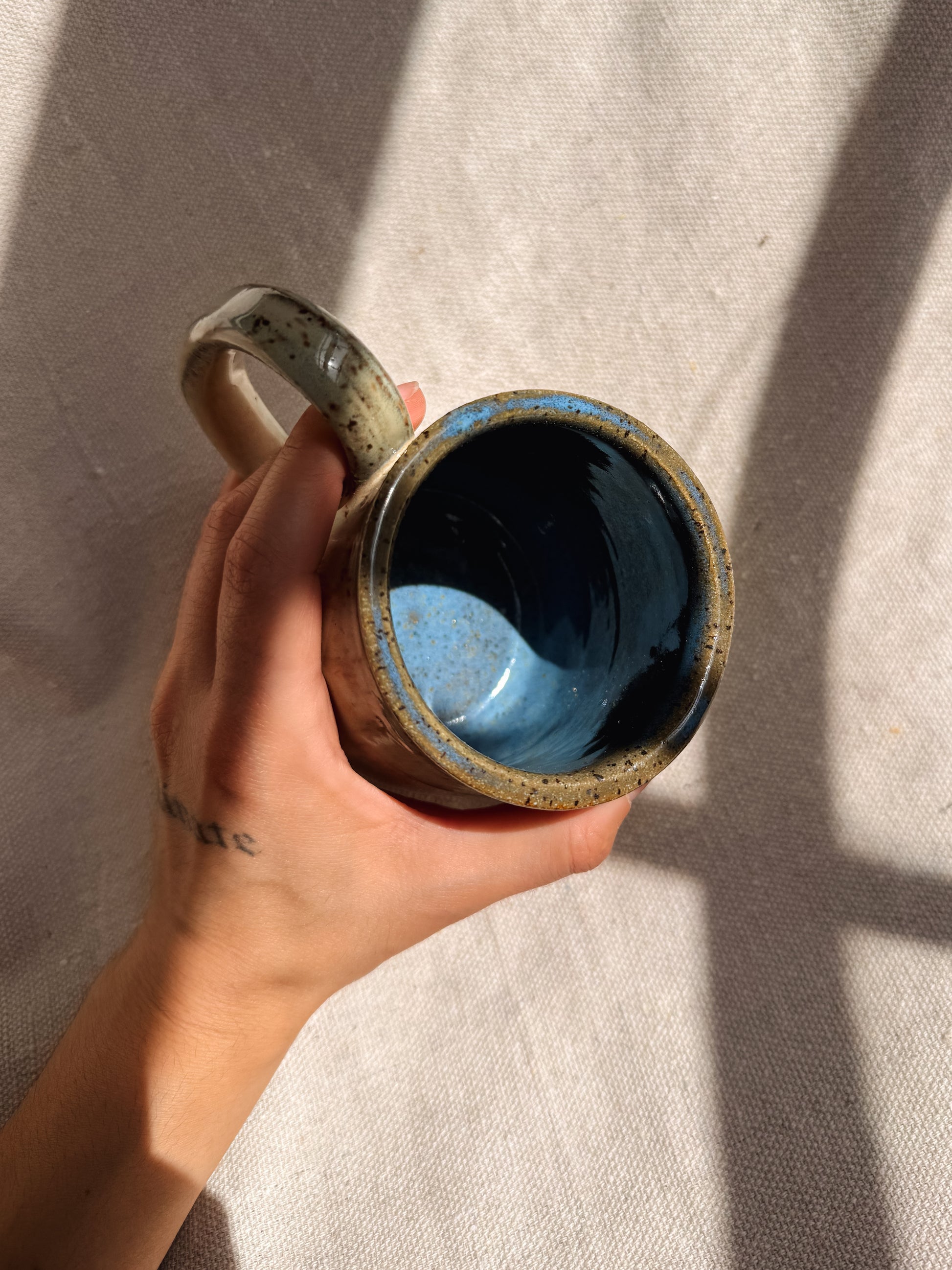 Hand holding a ceramic mug with blue interior against a neutral background