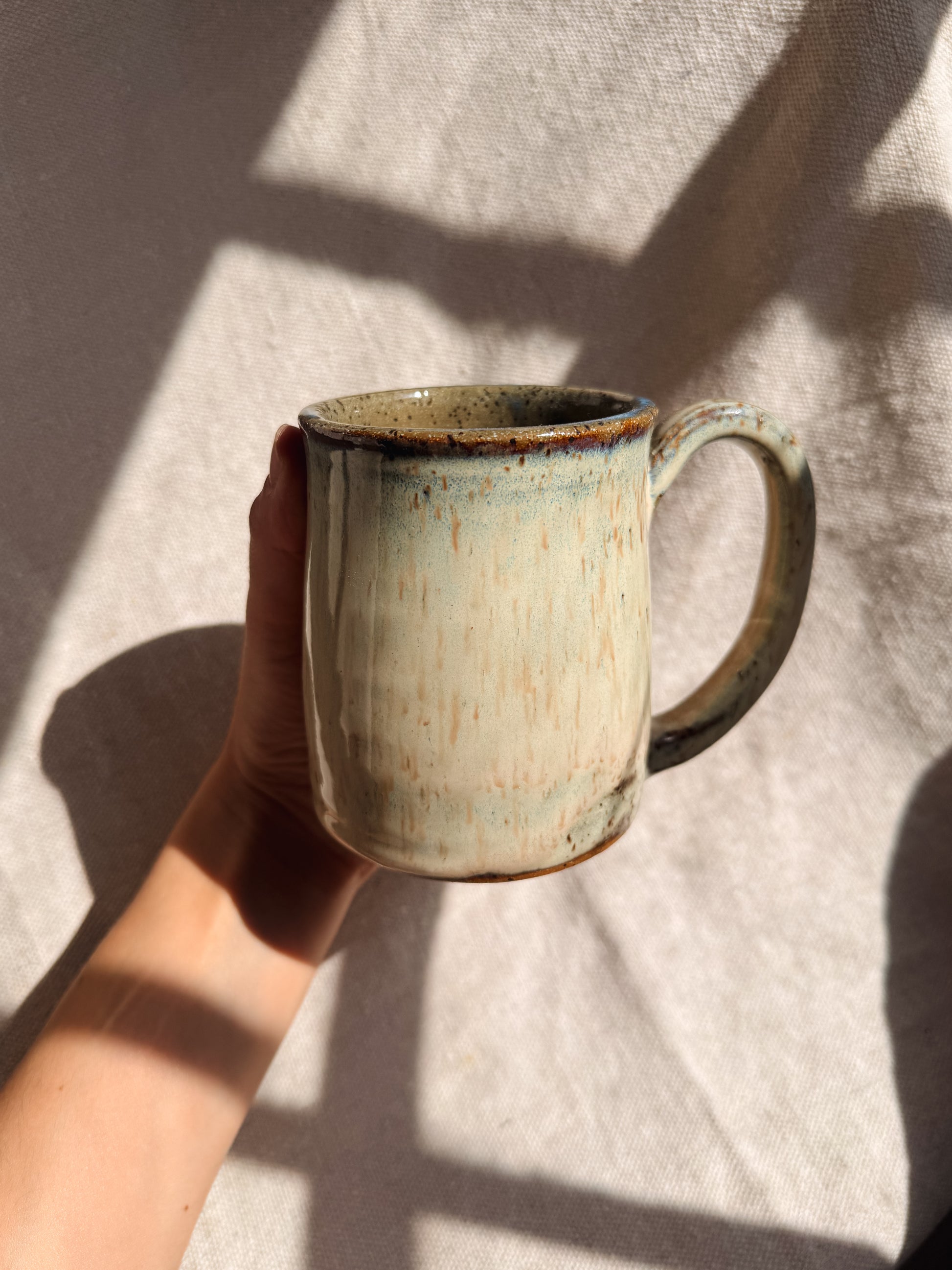 Hand holding a ceramic mug with a textured surface on a light fabric background
