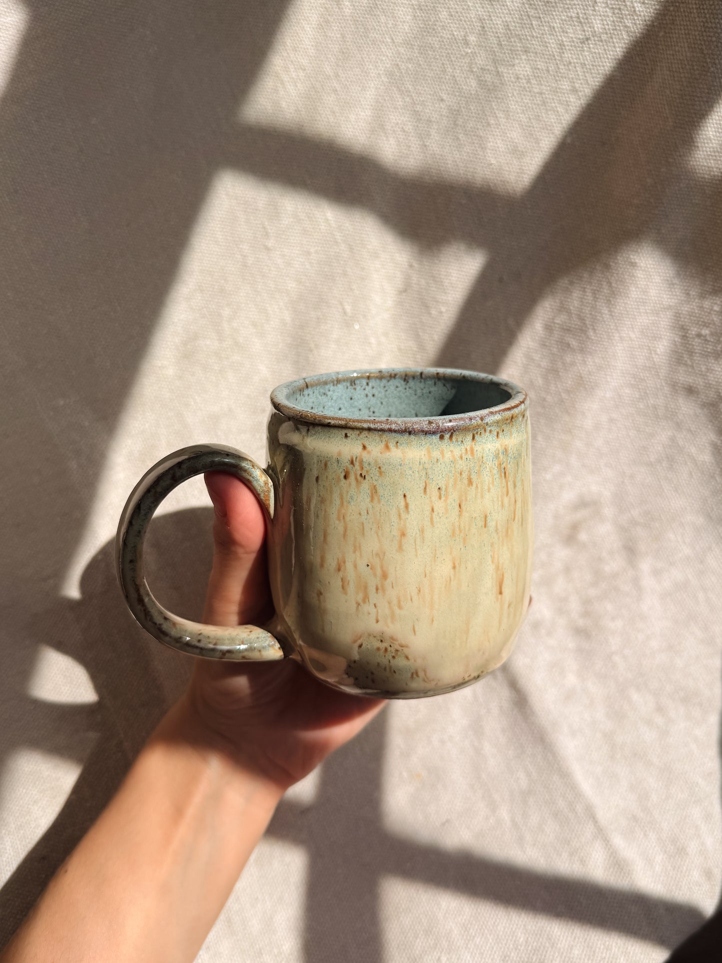 Hand holding a ceramic mug with a textured surface against a neutral background