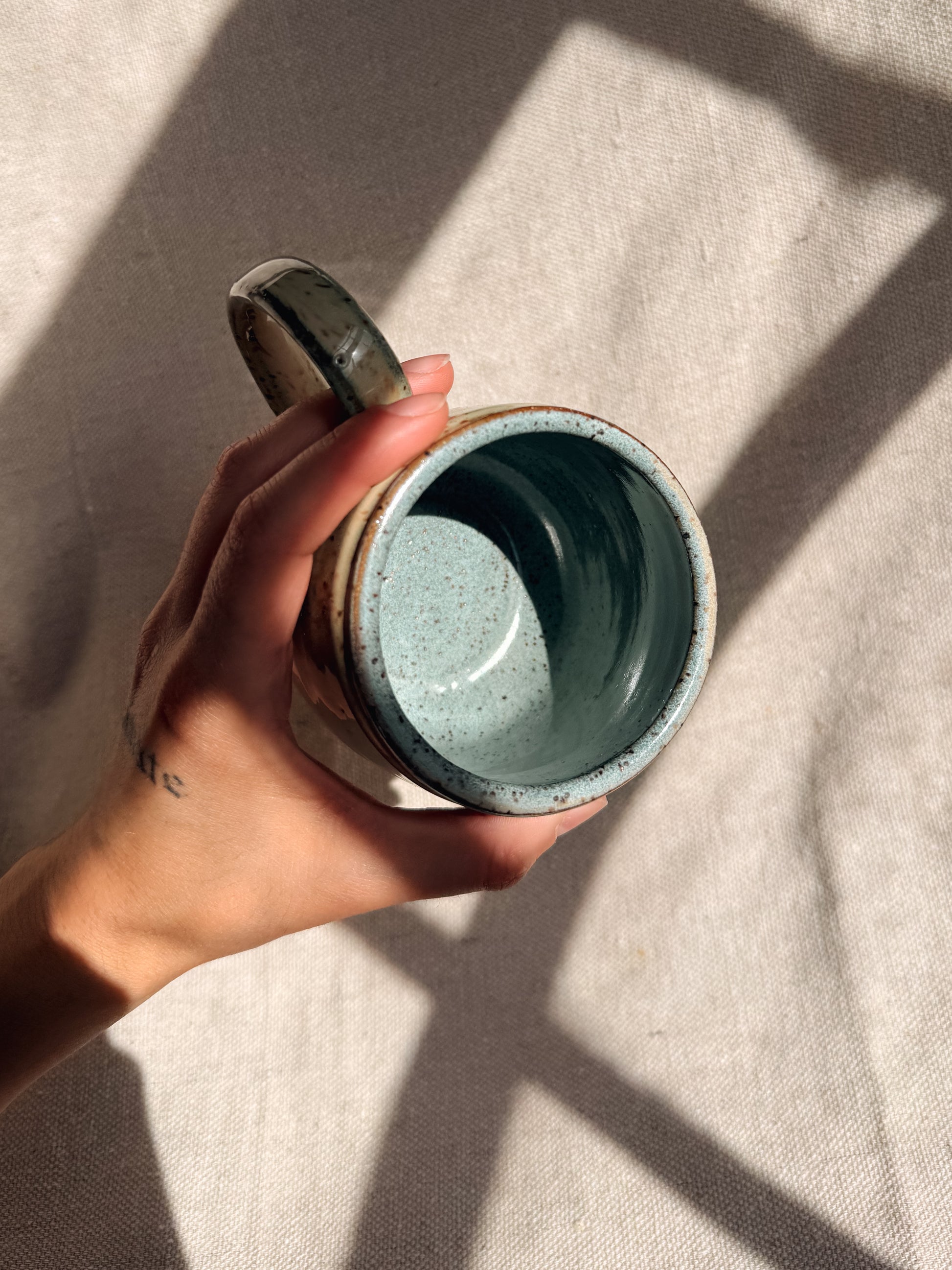 Hand holding a ceramic mug with a textured surface on a light fabric background