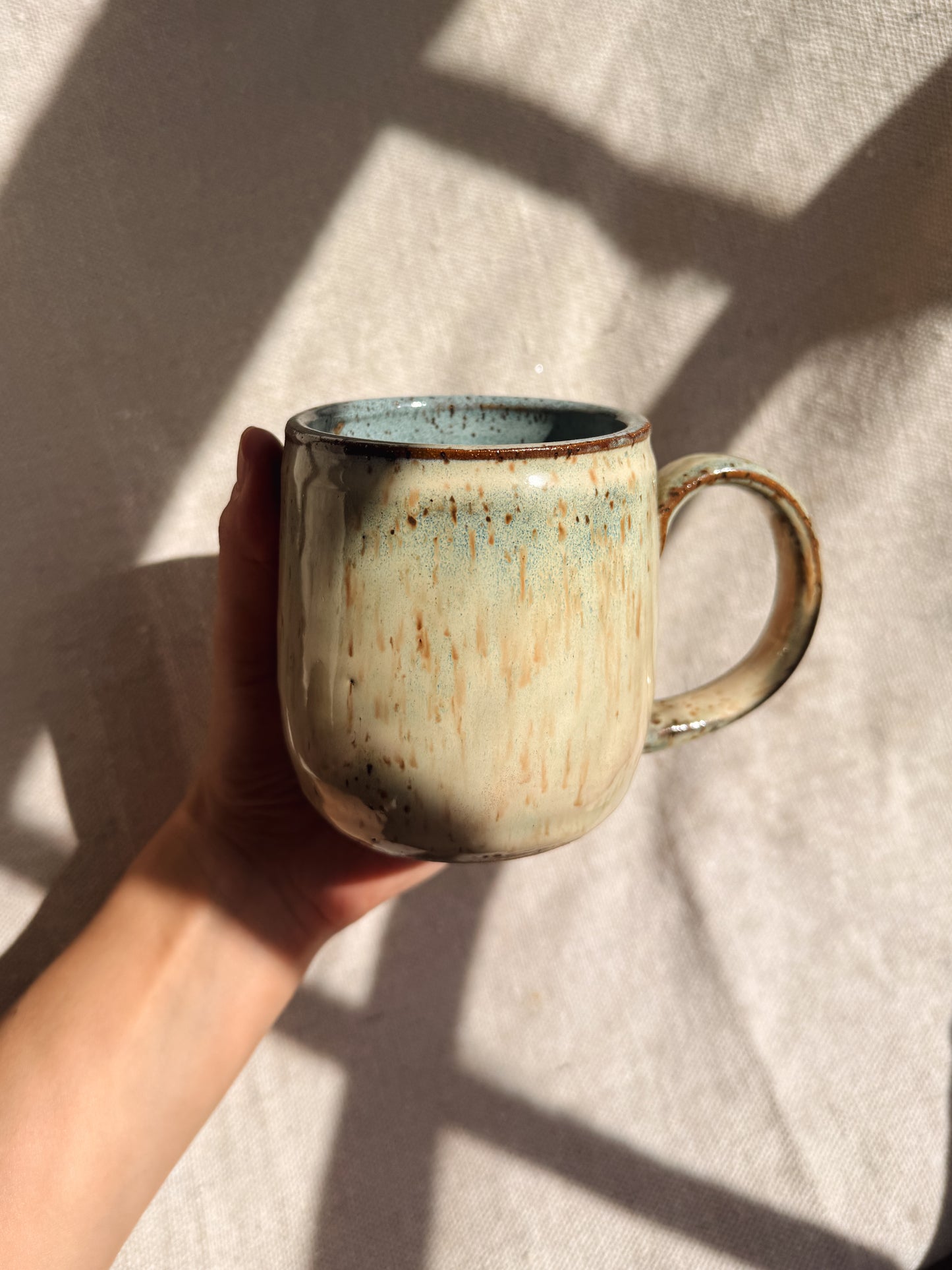 Hand holding a ceramic mug with a textured surface on a light background