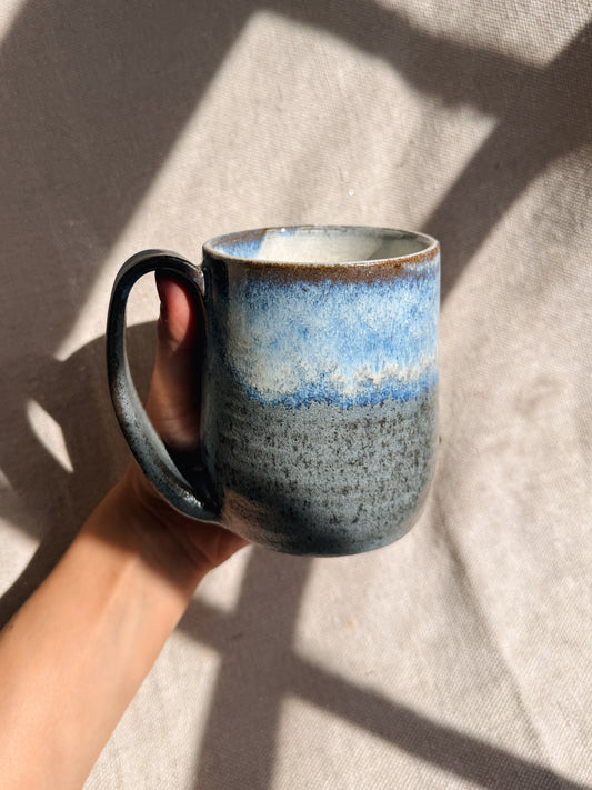 Hand holding a ceramic mug with blue and gray speckled design against a neutral background