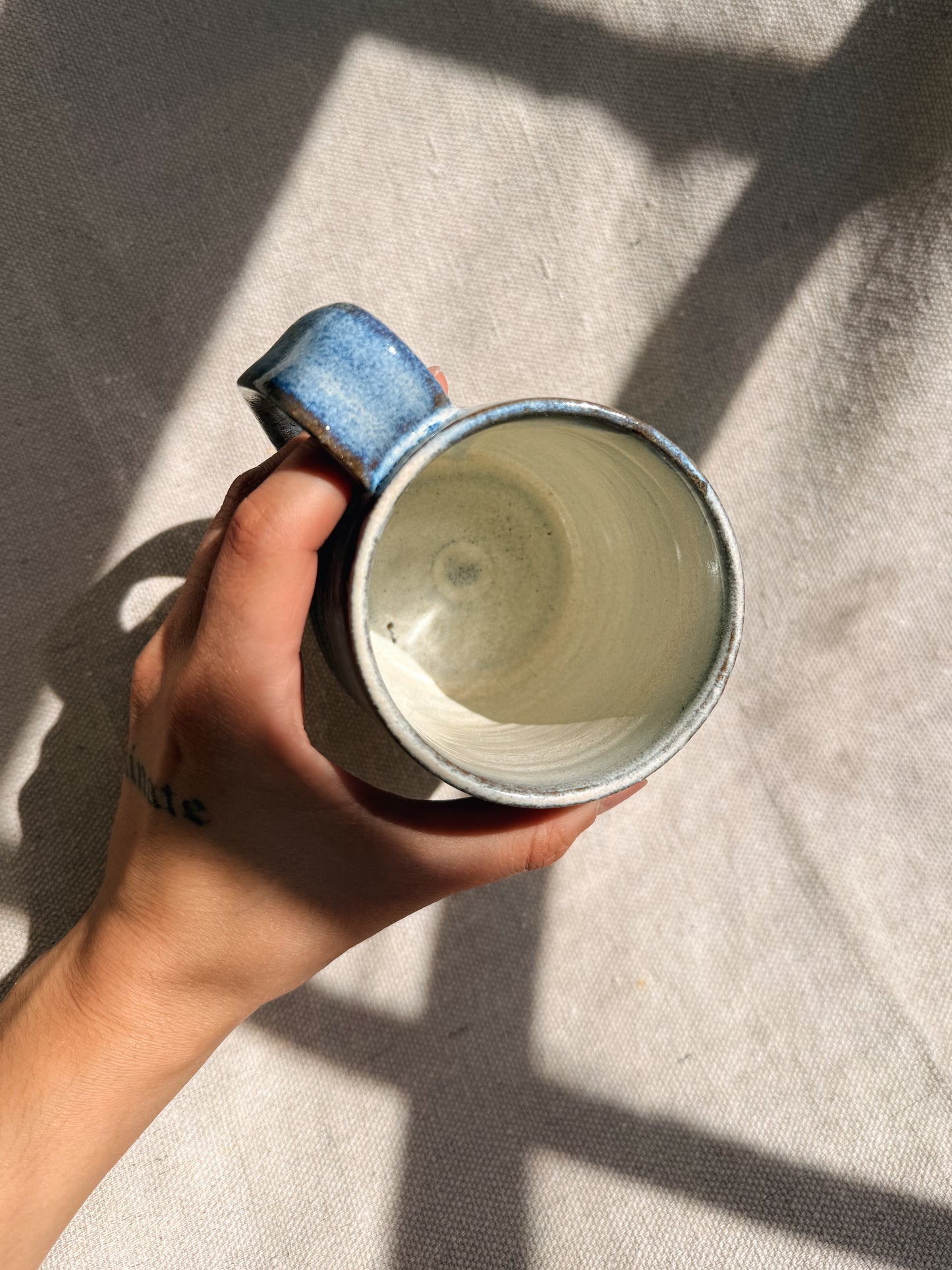 Hand holding a ceramic mug with a blue handle on a textured surface