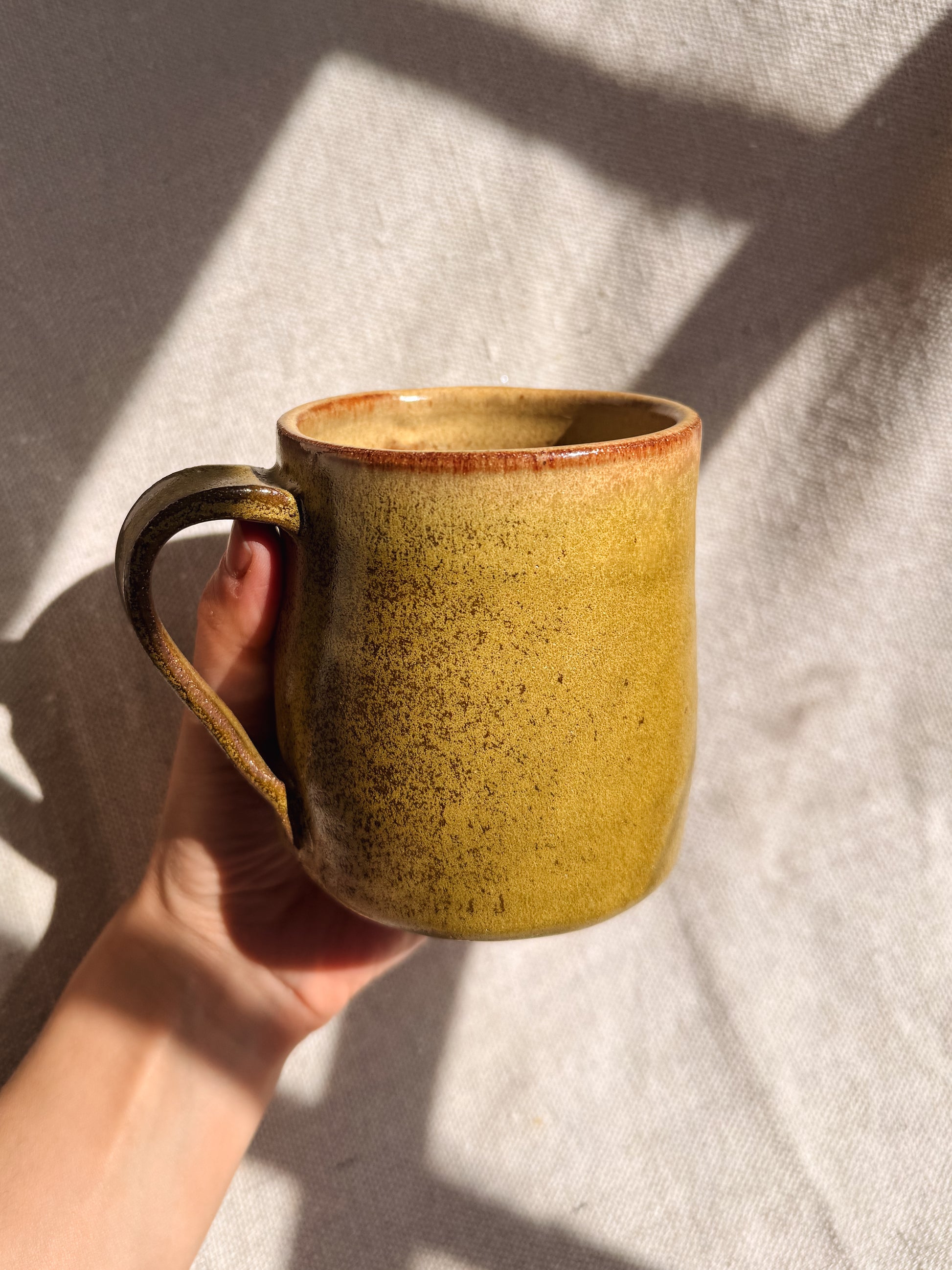 Hand holding a ceramic mug with a textured surface against a neutral background