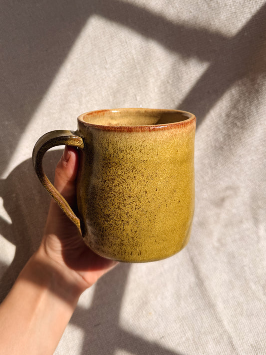 Hand holding a ceramic mug with a textured surface against a neutral background