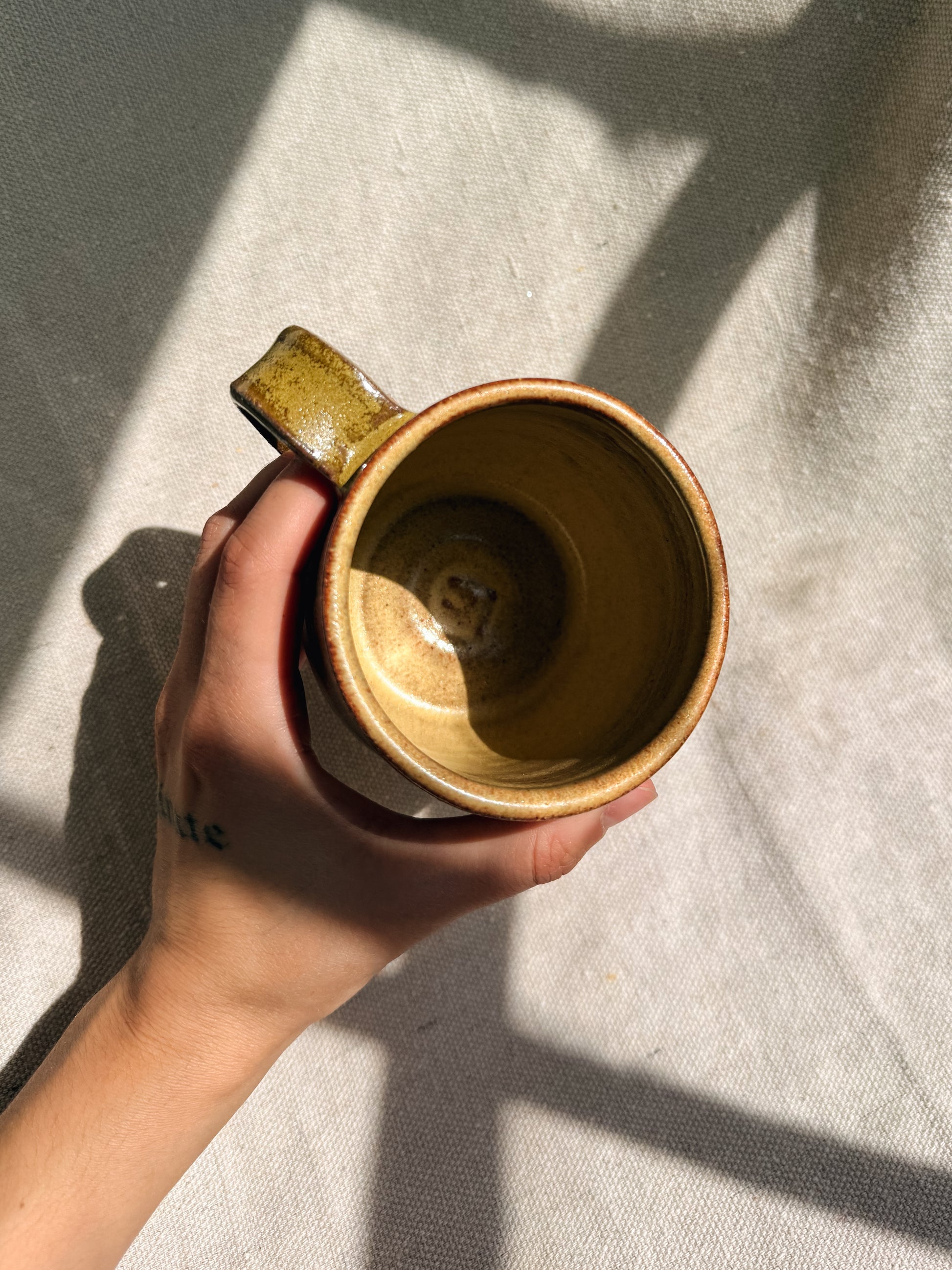 Hand holding a brown ceramic mug on a textured surface