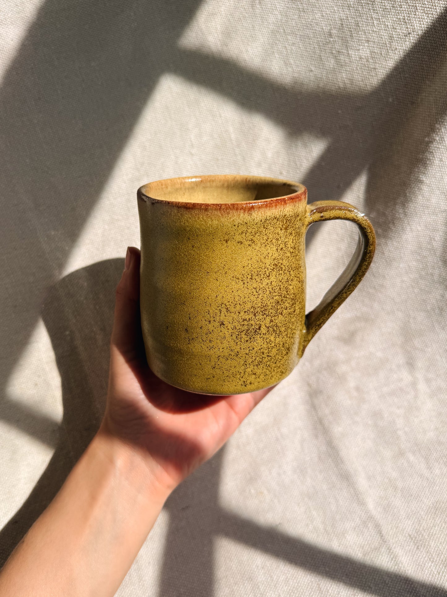 Hand holding a yellow ceramic mug against a neutral background