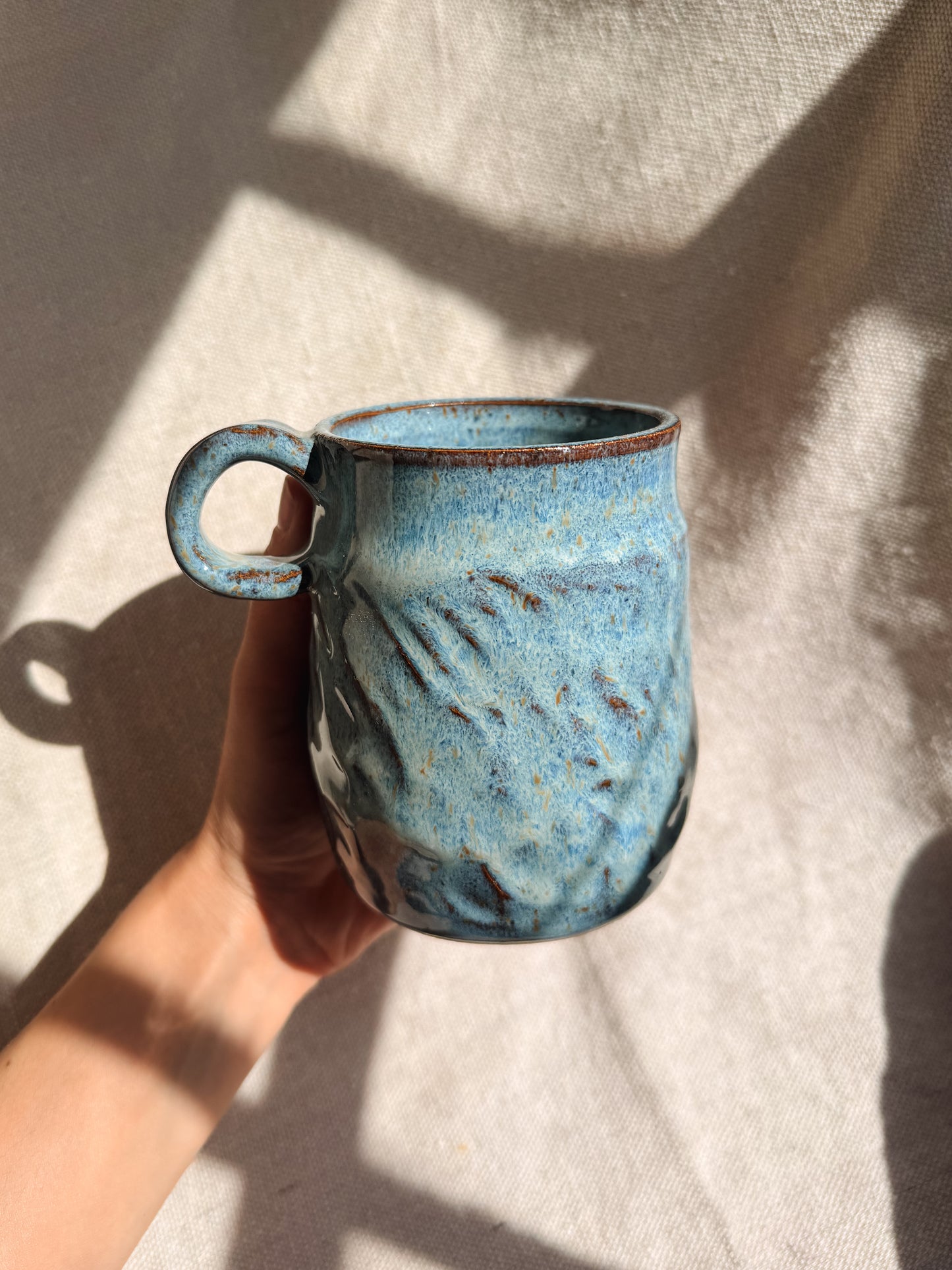 Hand holding a blue ceramic mug against a neutral background