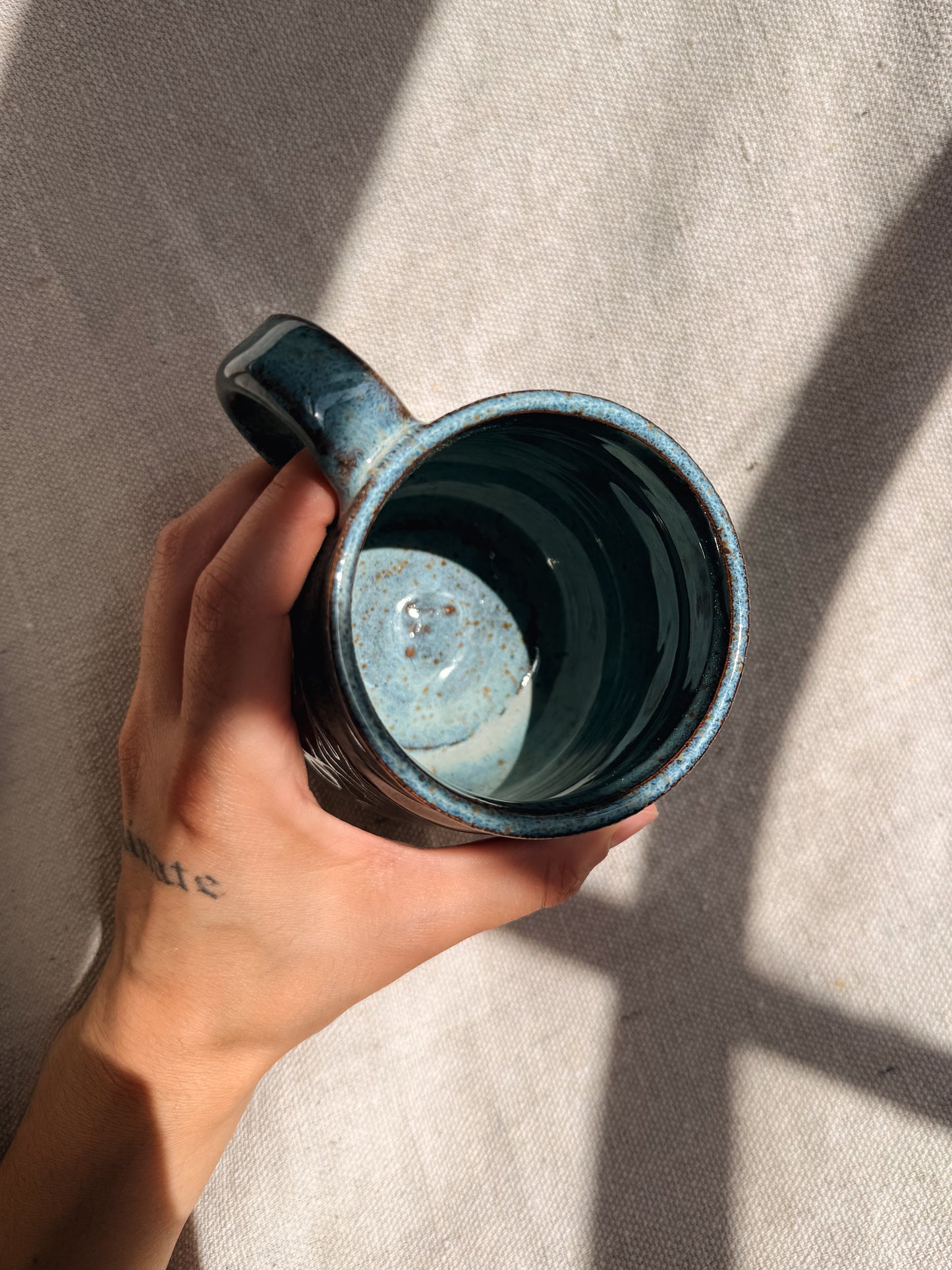 Hand holding a blue ceramic mug against a neutral background