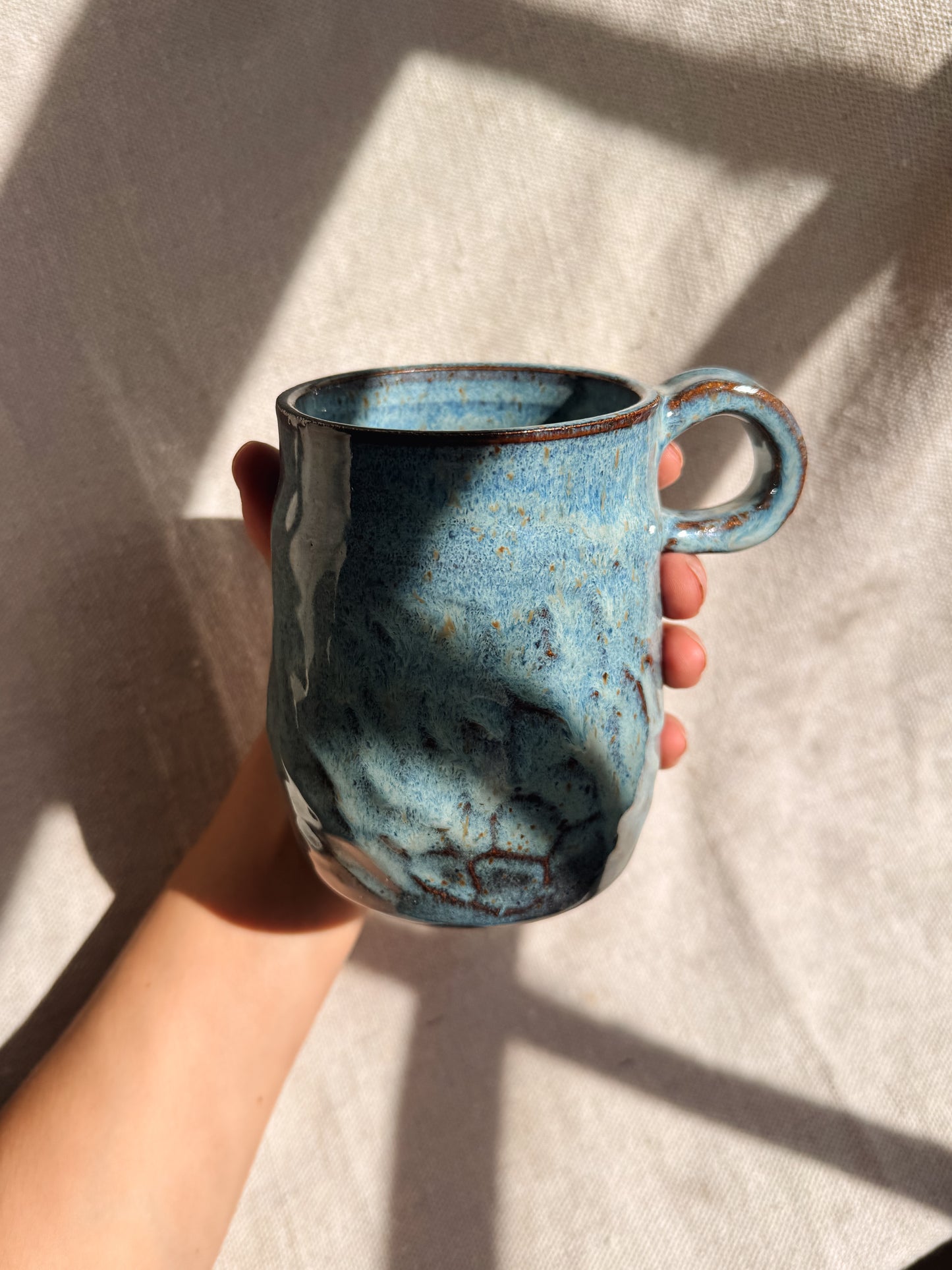 Hand holding a blue ceramic mug against a light background