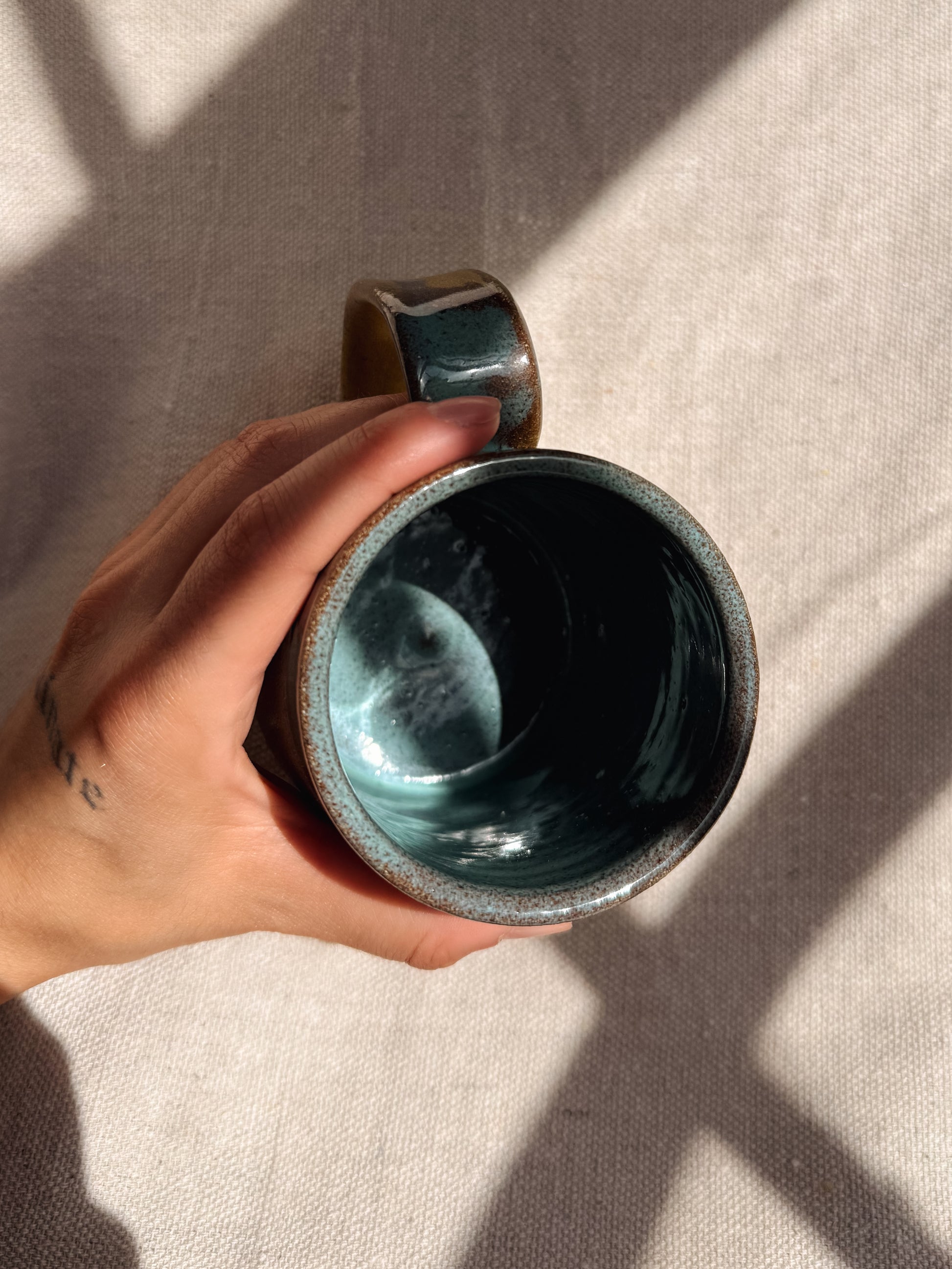 Hand holding a ceramic mug with a textured surface on a neutral background