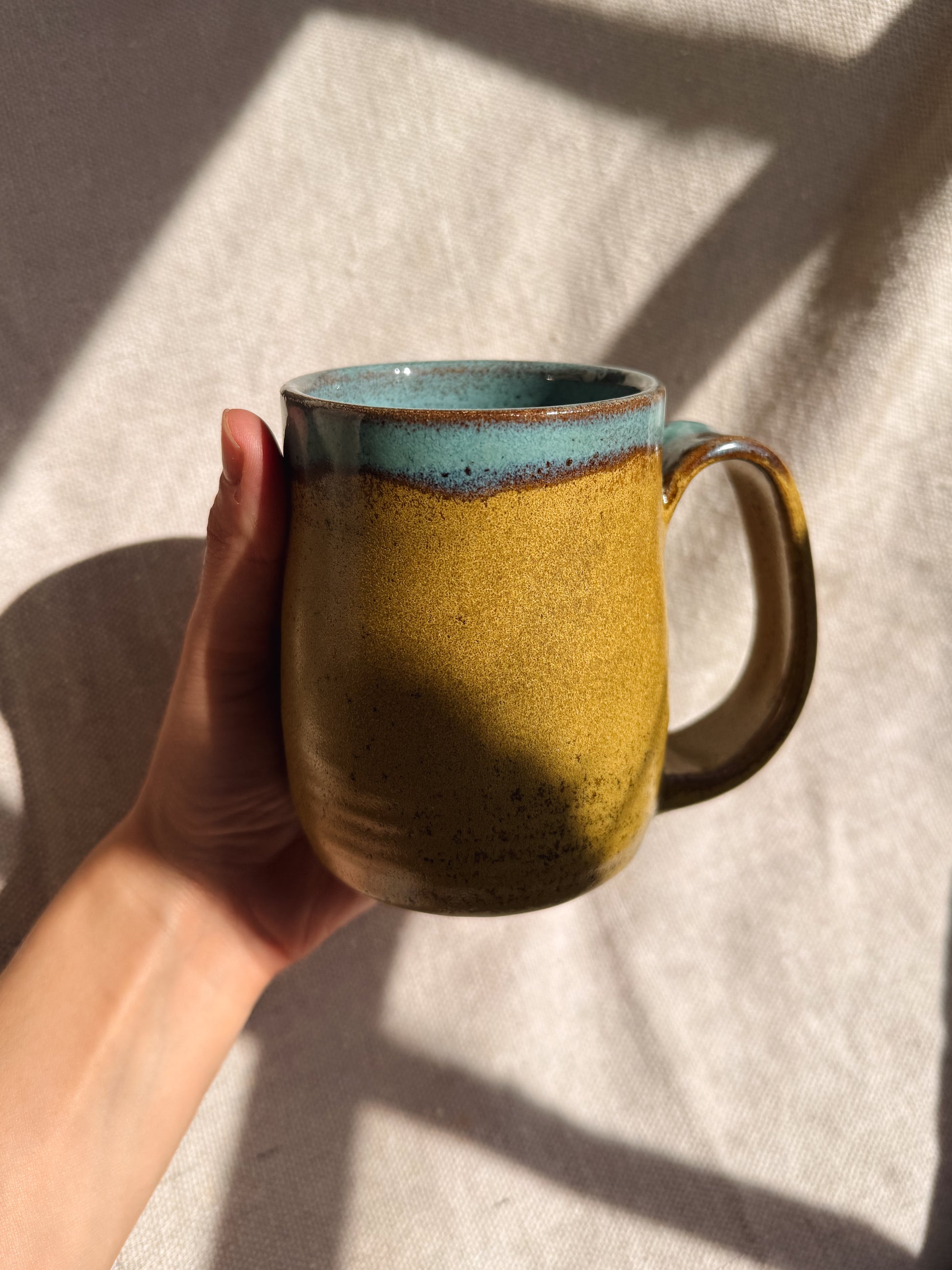 Hand holding a ceramic mug with a textured surface and blue rim on a light background