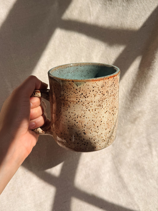 Hand holding a ceramic mug with speckled design on a neutral background