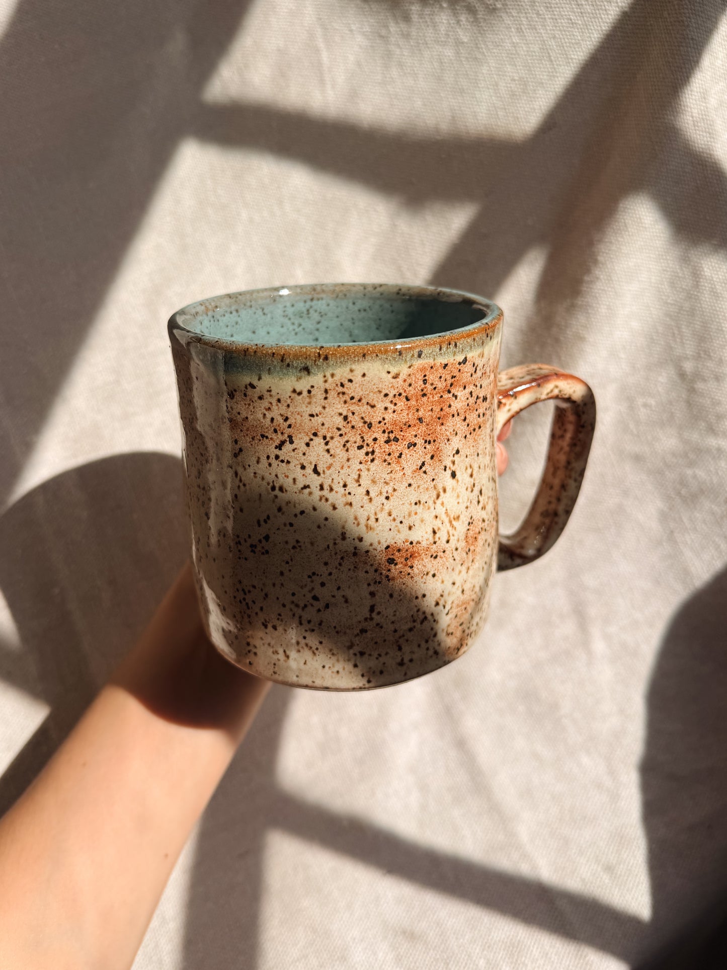 Speckled ceramic mug held by a hand on a light fabric background