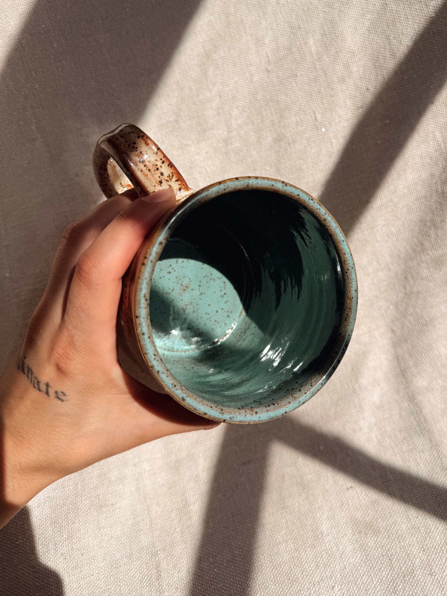Hand holding a ceramic mug with a textured surface on a neutral background