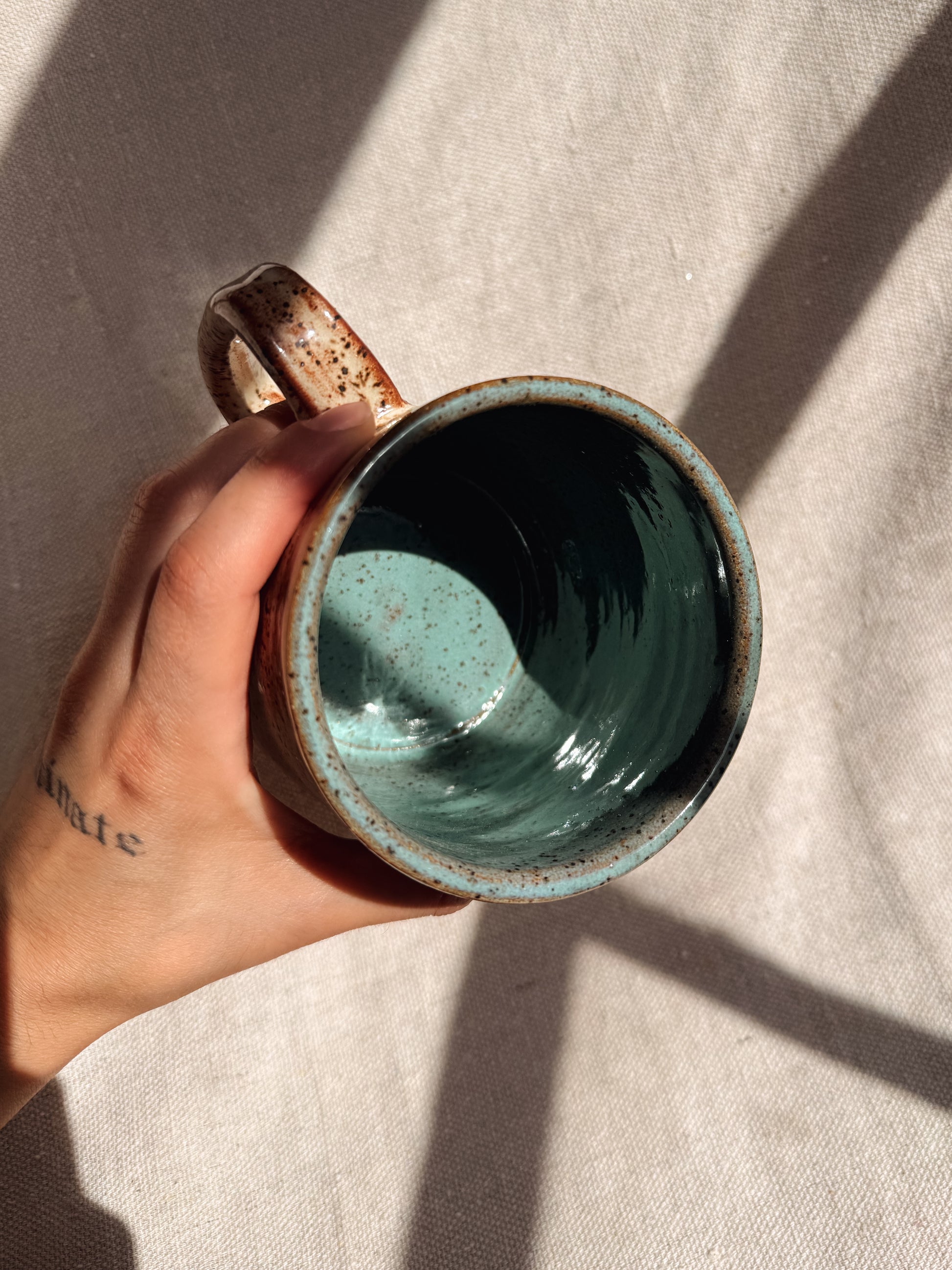Hand holding a ceramic mug with a textured surface on a neutral background