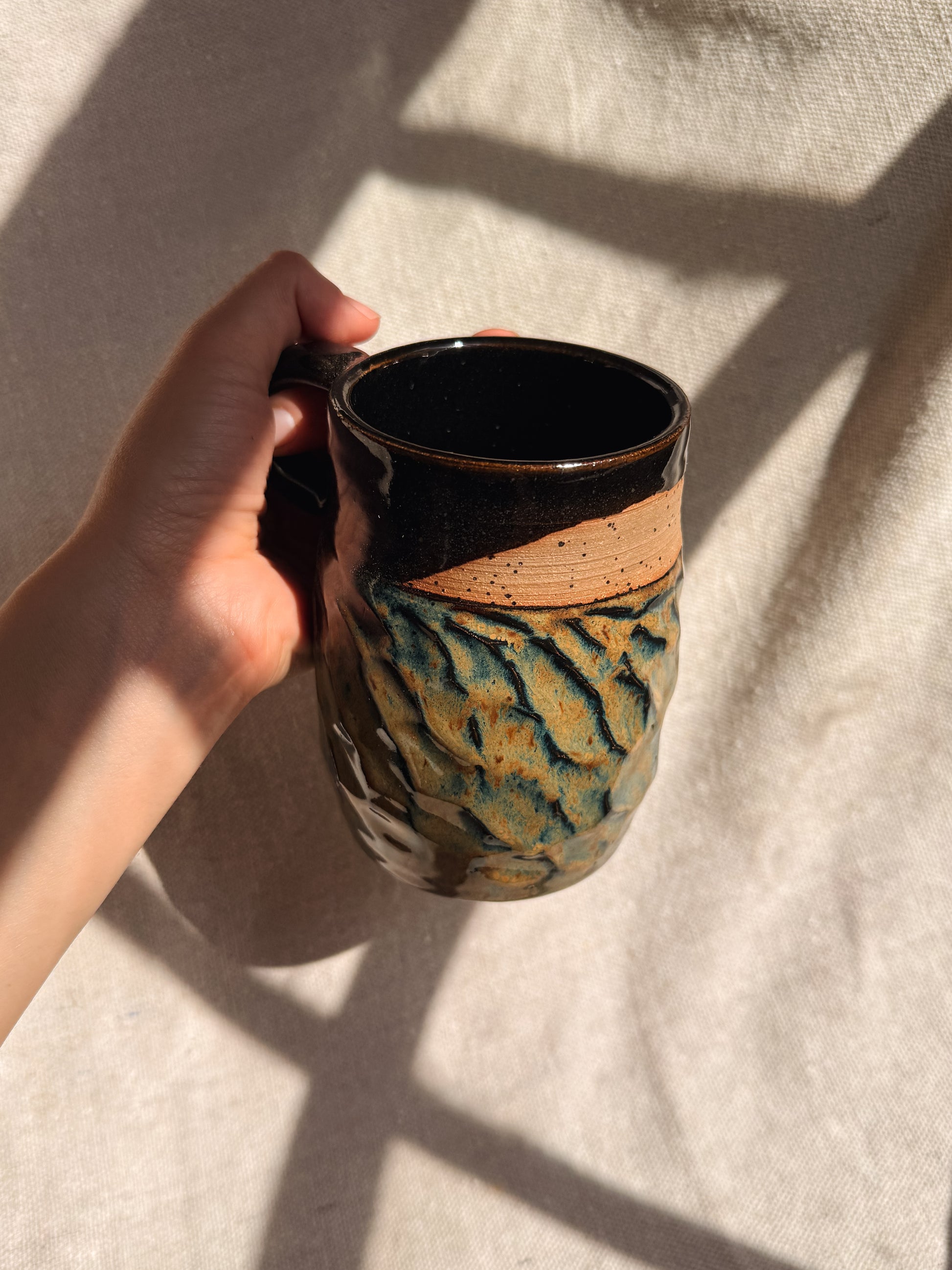 Hand holding a ceramic mug with a unique pattern on a light background