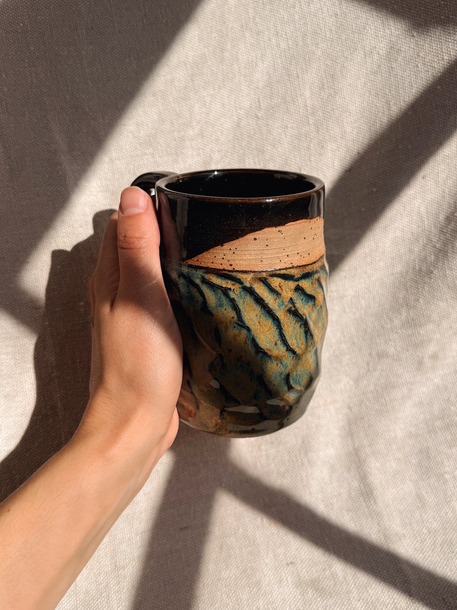 Hand holding a ceramic mug with artistic design on a textured surface