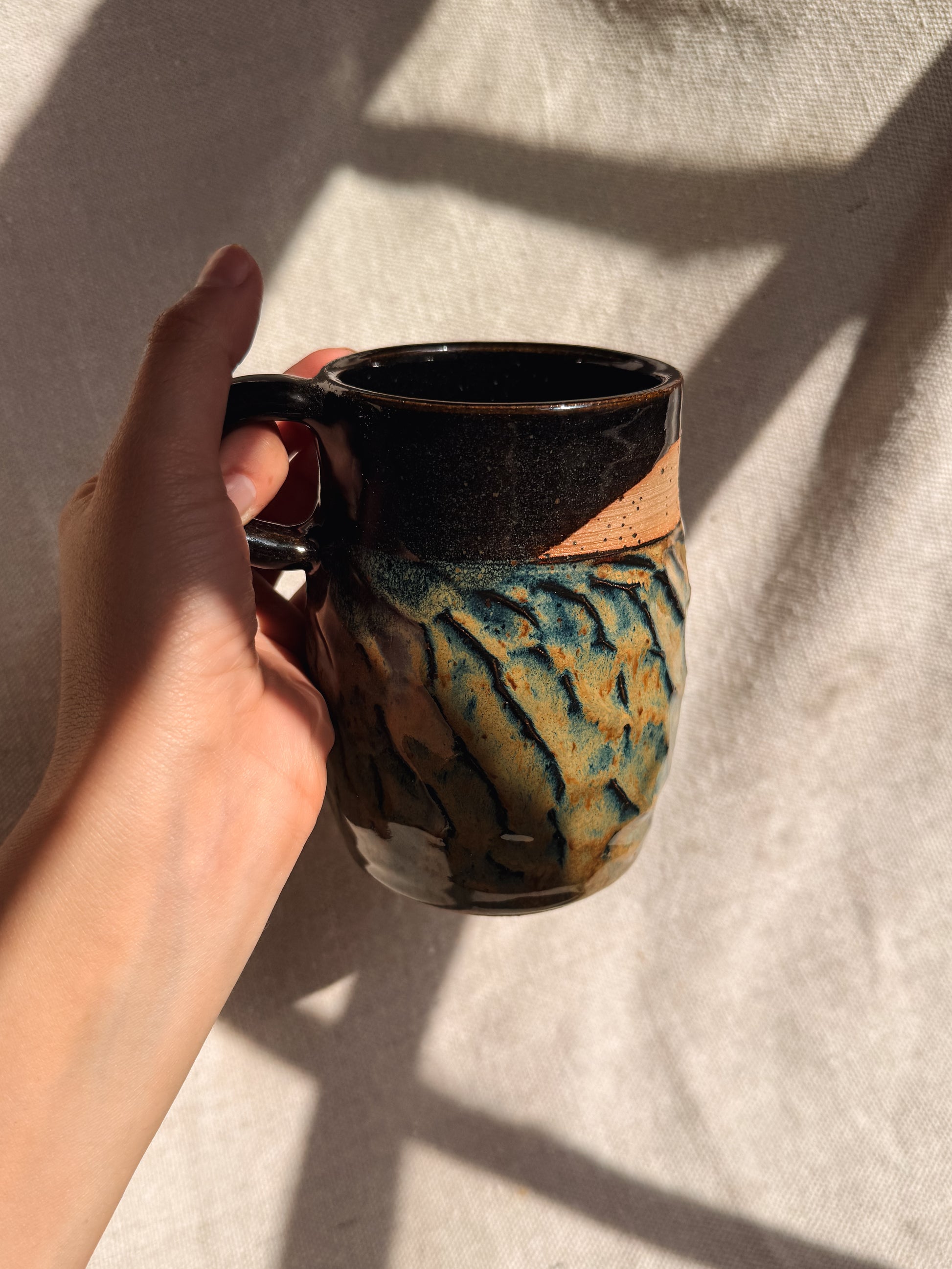 Hand holding a ceramic mug with a tiger stripe pattern on a neutral background