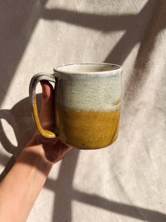 Hand holding a ceramic mug with a gradient design on a neutral background