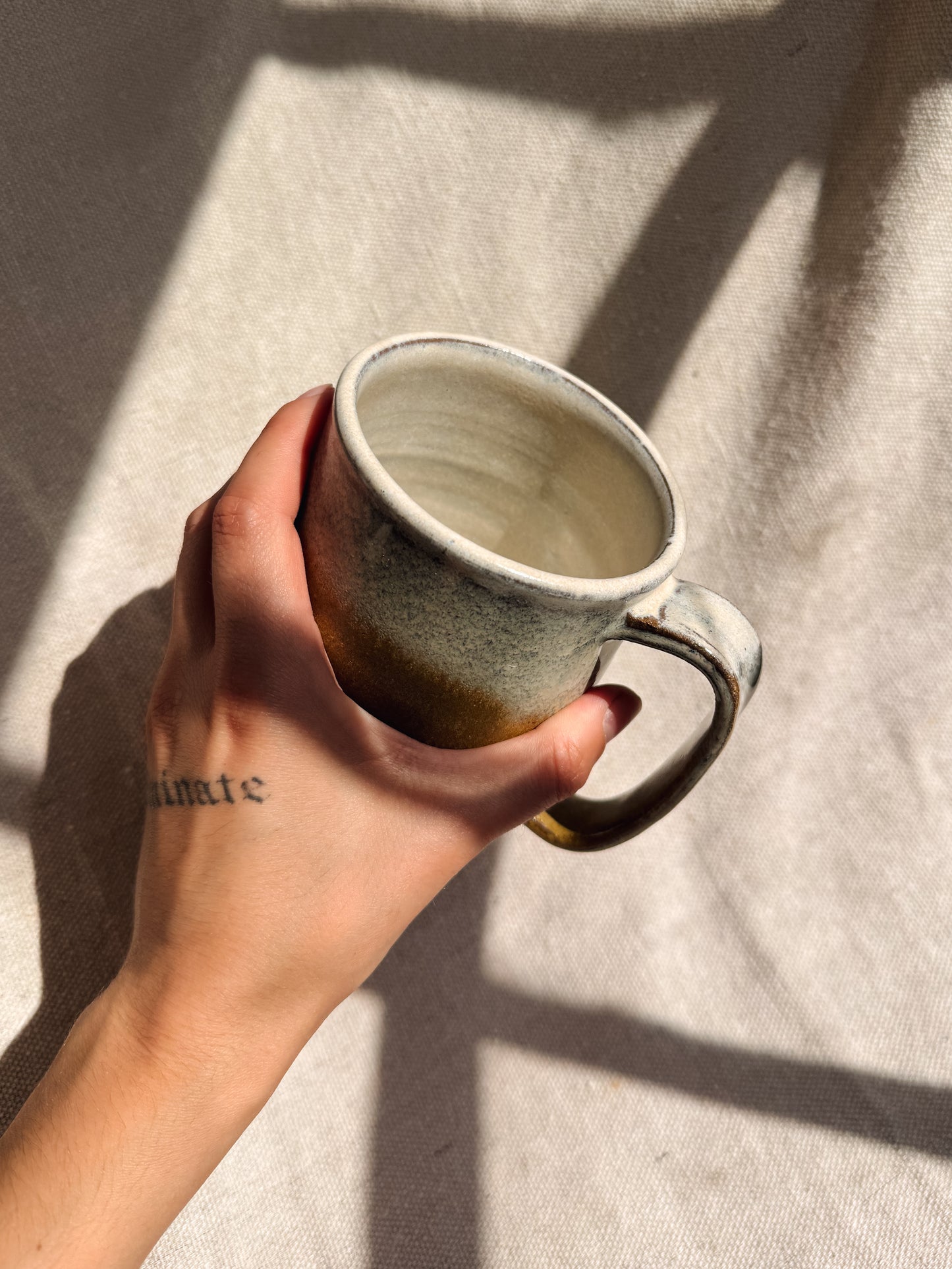 Hand holding a ceramic mug against a textured fabric background