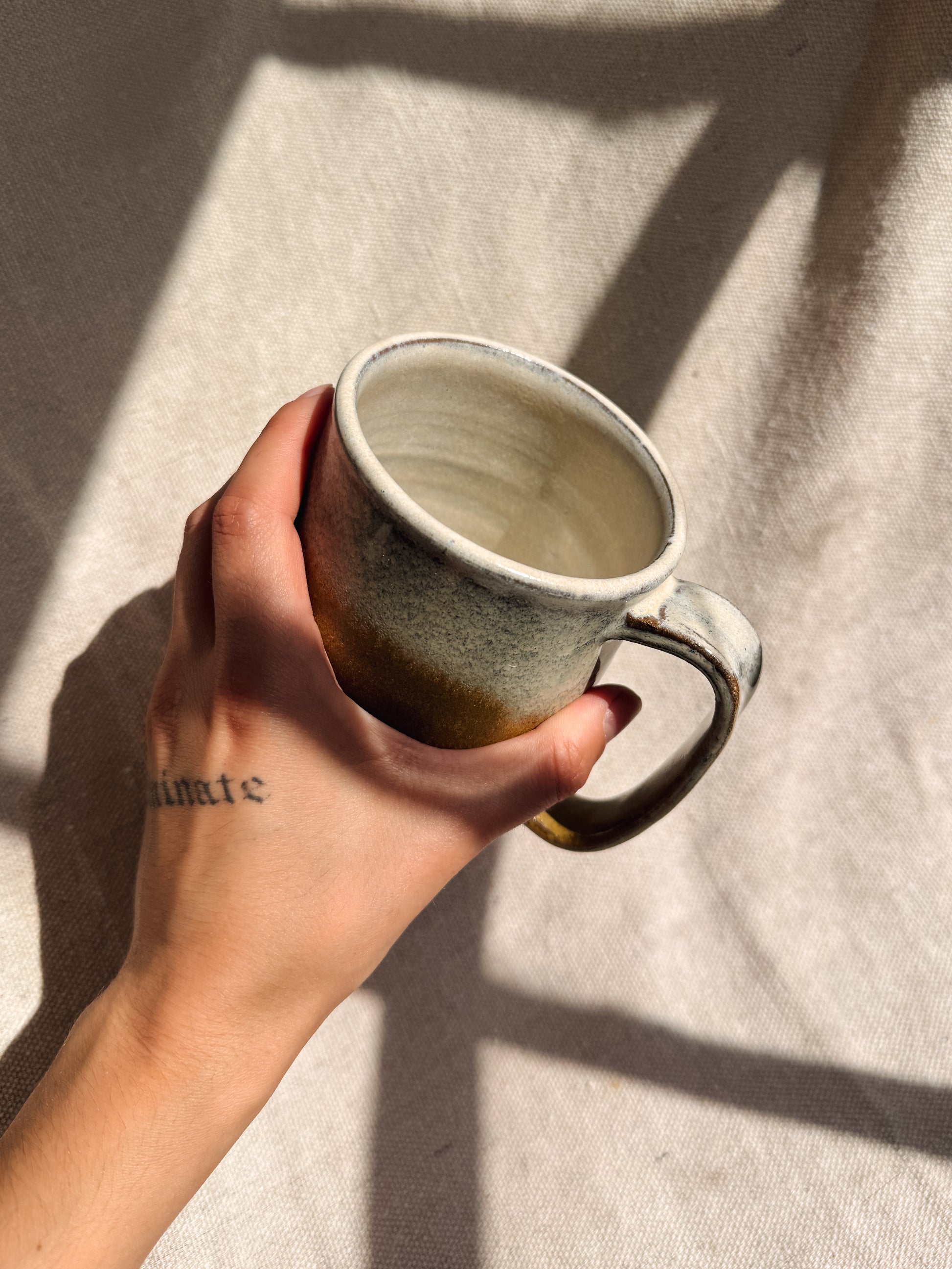 Hand holding a ceramic mug against a textured fabric background