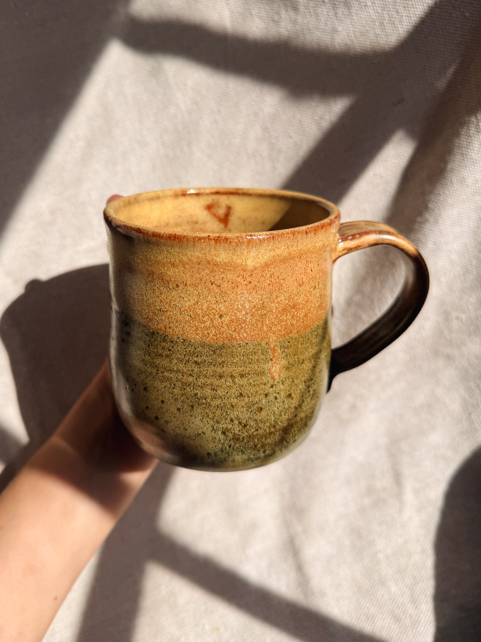 Hand holding a ceramic mug with two-tone design on a light fabric background