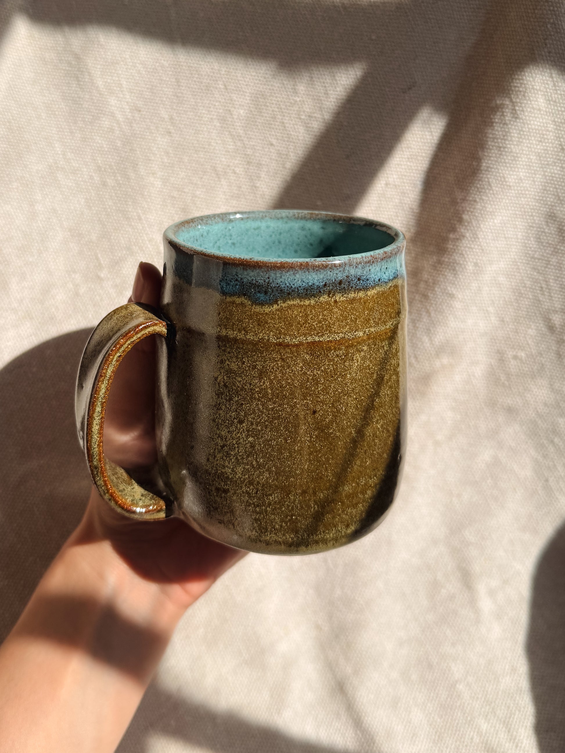 Hand holding a ceramic mug with a textured surface and blue interior against a light background