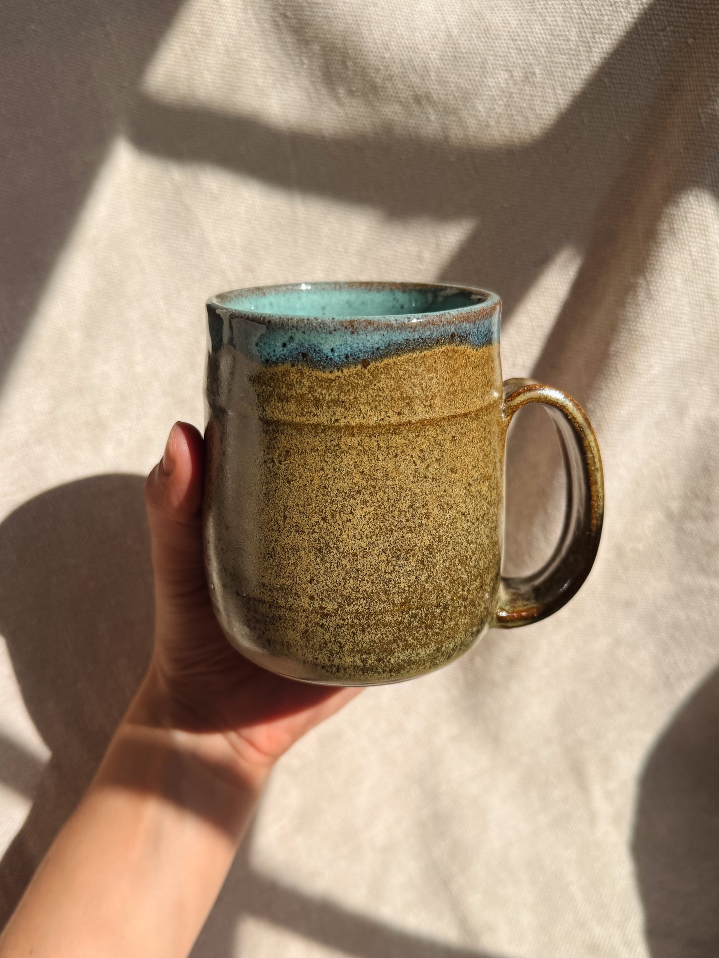 Hand holding a ceramic mug with a textured surface and blue interior against a neutral background
