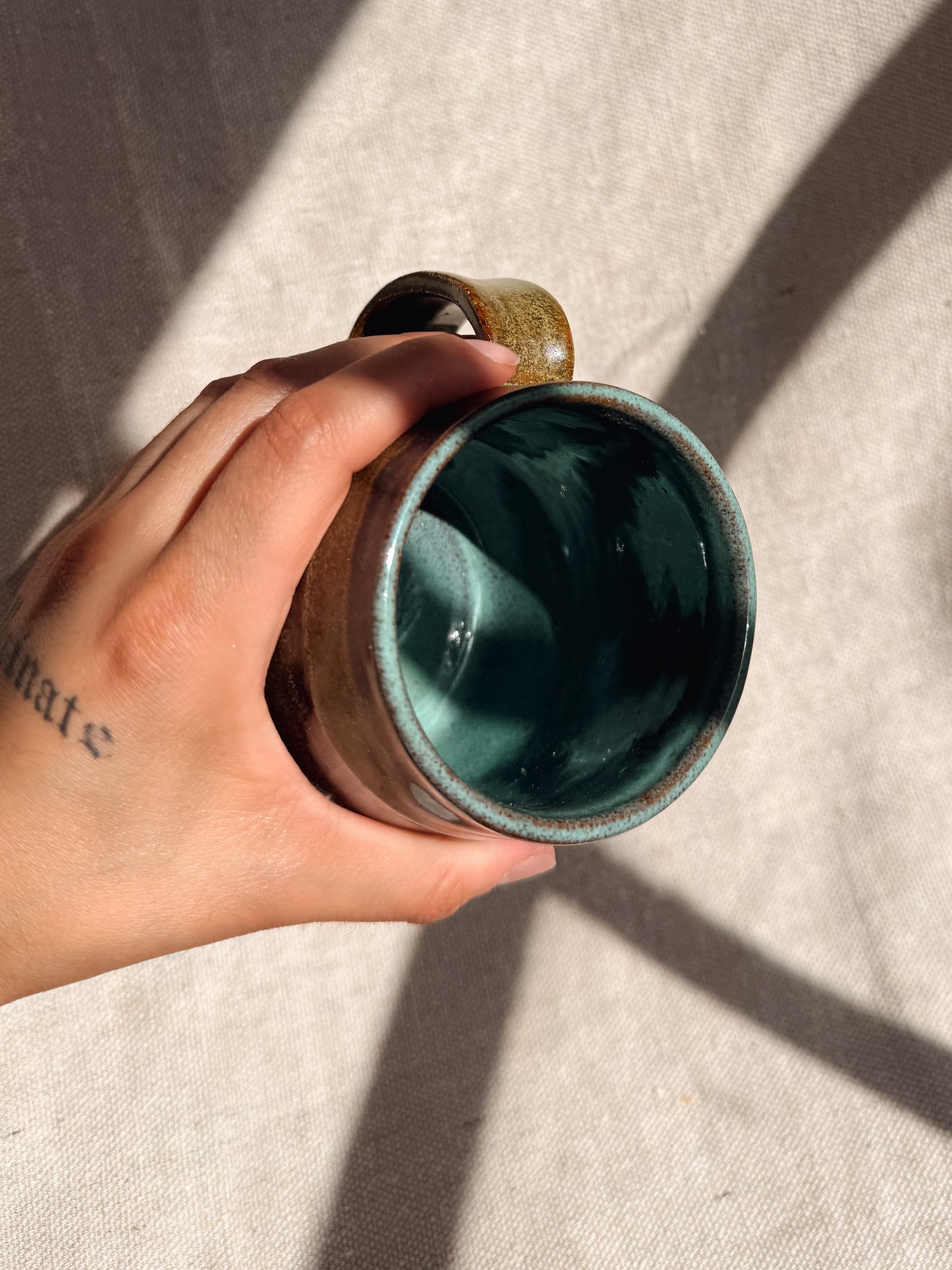 Hand holding a ceramic mug with a green interior on a beige surface