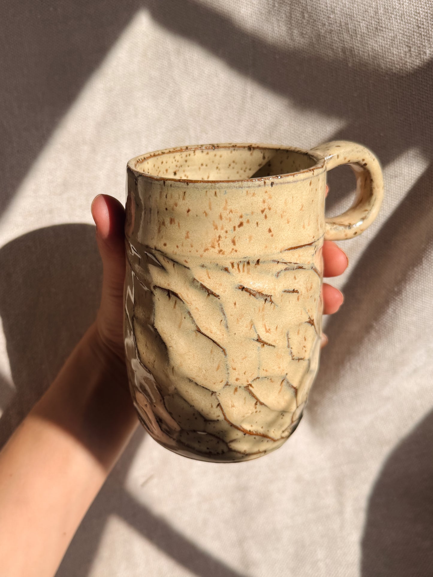 Hand holding a textured ceramic mug against a neutral background