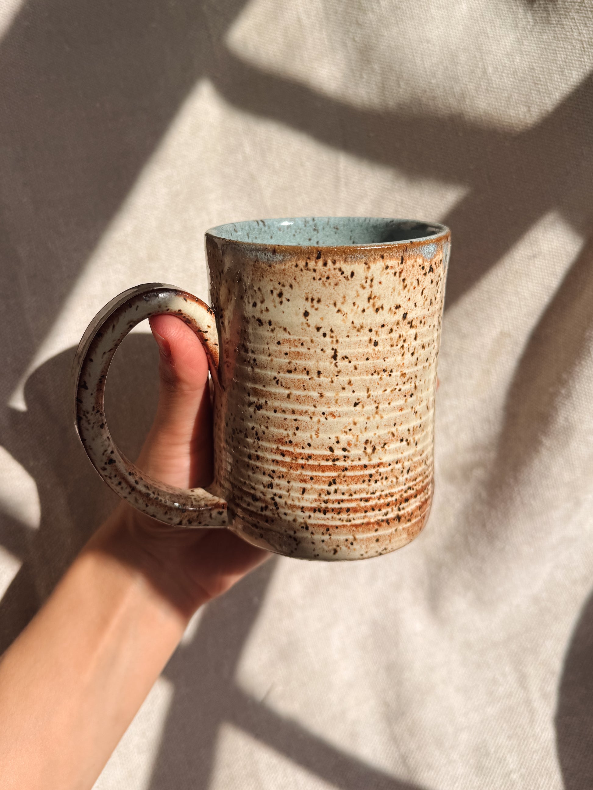 Hand holding a ceramic mug with a textured surface against a neutral background