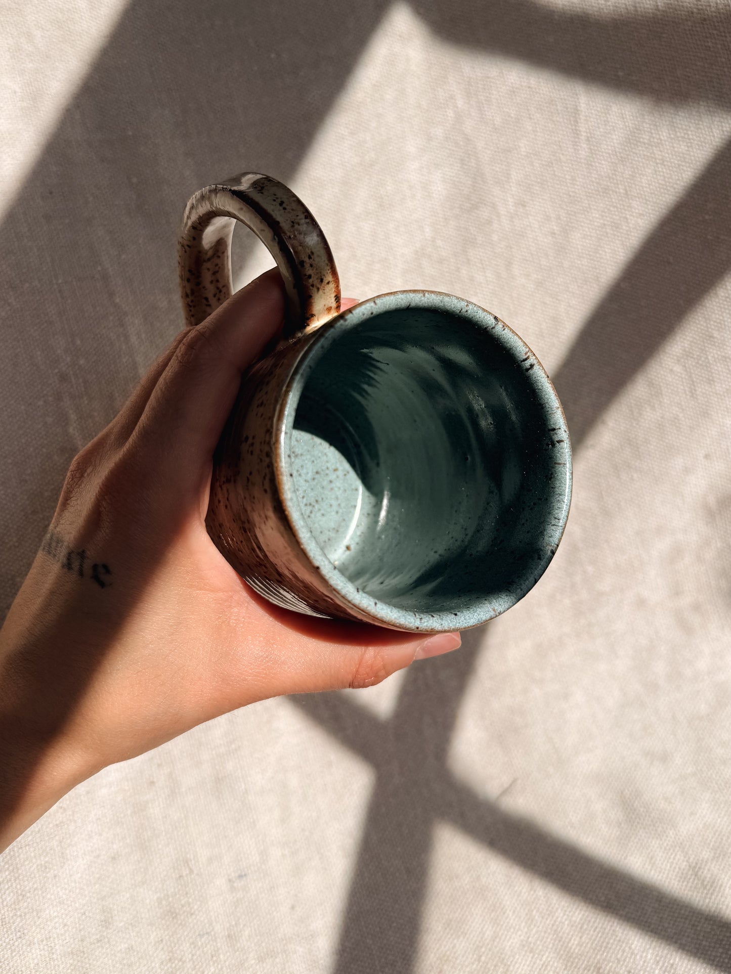 Hand holding a ceramic mug with a textured surface on a neutral background