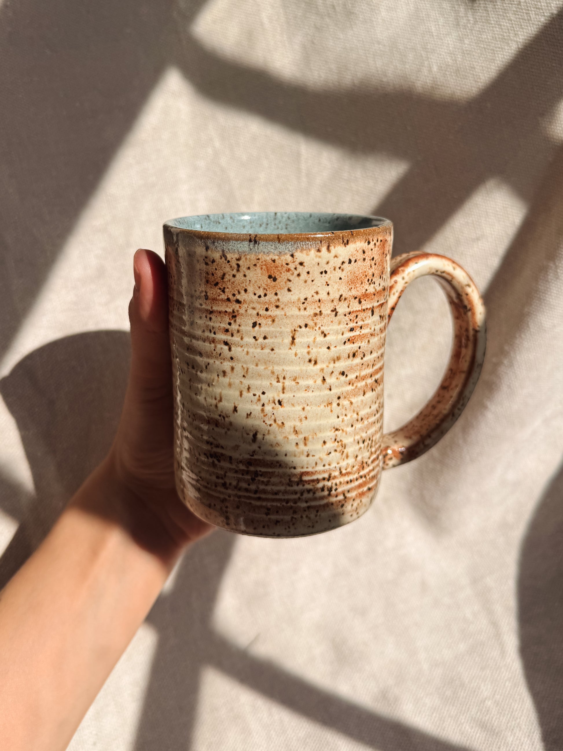 Hand holding a ceramic mug with speckled design on a light background