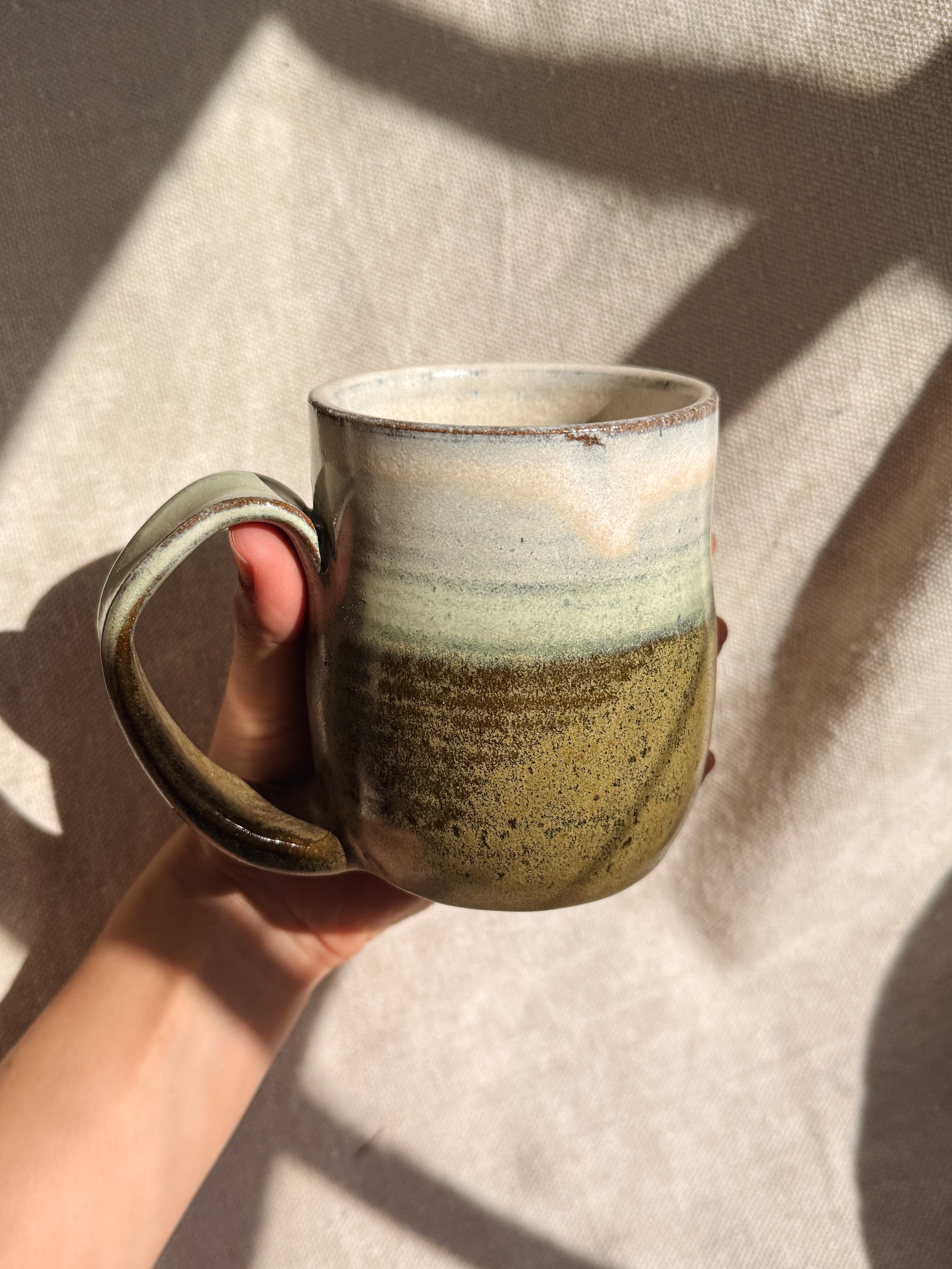Hand holding a ceramic mug with a textured surface against a neutral background