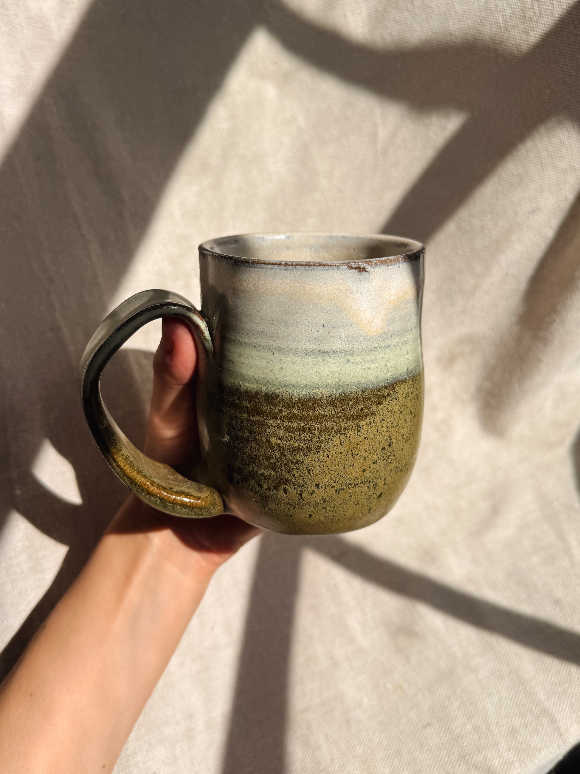 Hand holding a ceramic mug with a textured surface against a neutral background