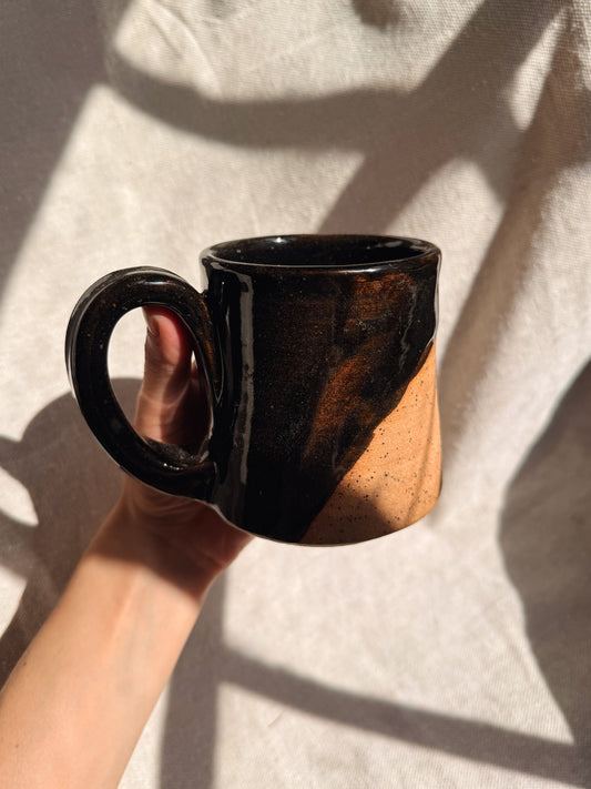 Hand holding a black and brown ceramic mug against a neutral background