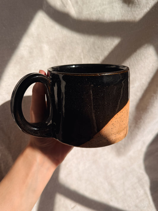 Black ceramic mug held by a hand against a neutral background