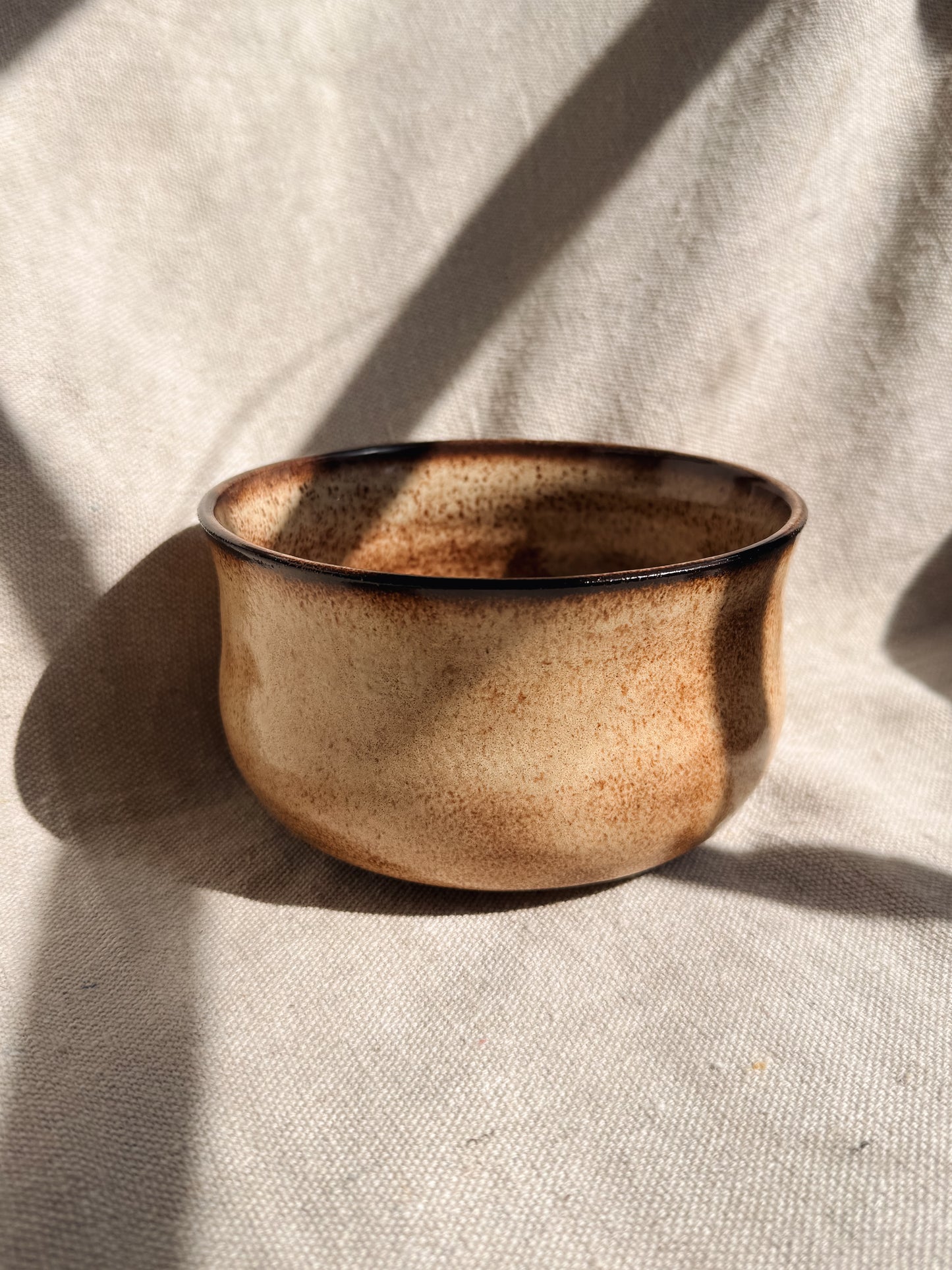 Ceramic bowl with brown speckles on a beige fabric background