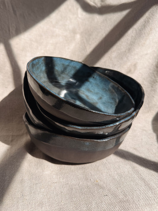 Stack of black ceramic bowls with blue interior on a beige fabric background
