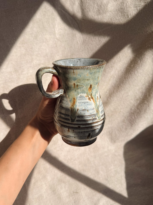 Hand holding a rustic ceramic mug against a neutral background