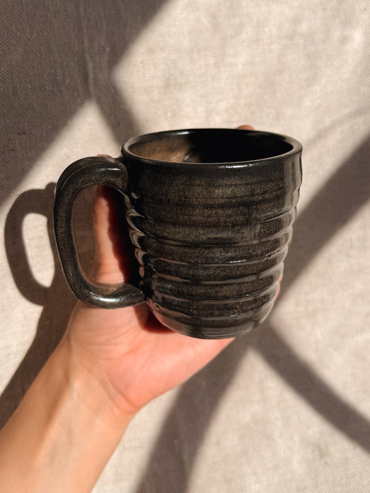 Hand holding a black ceramic mug against a neutral background