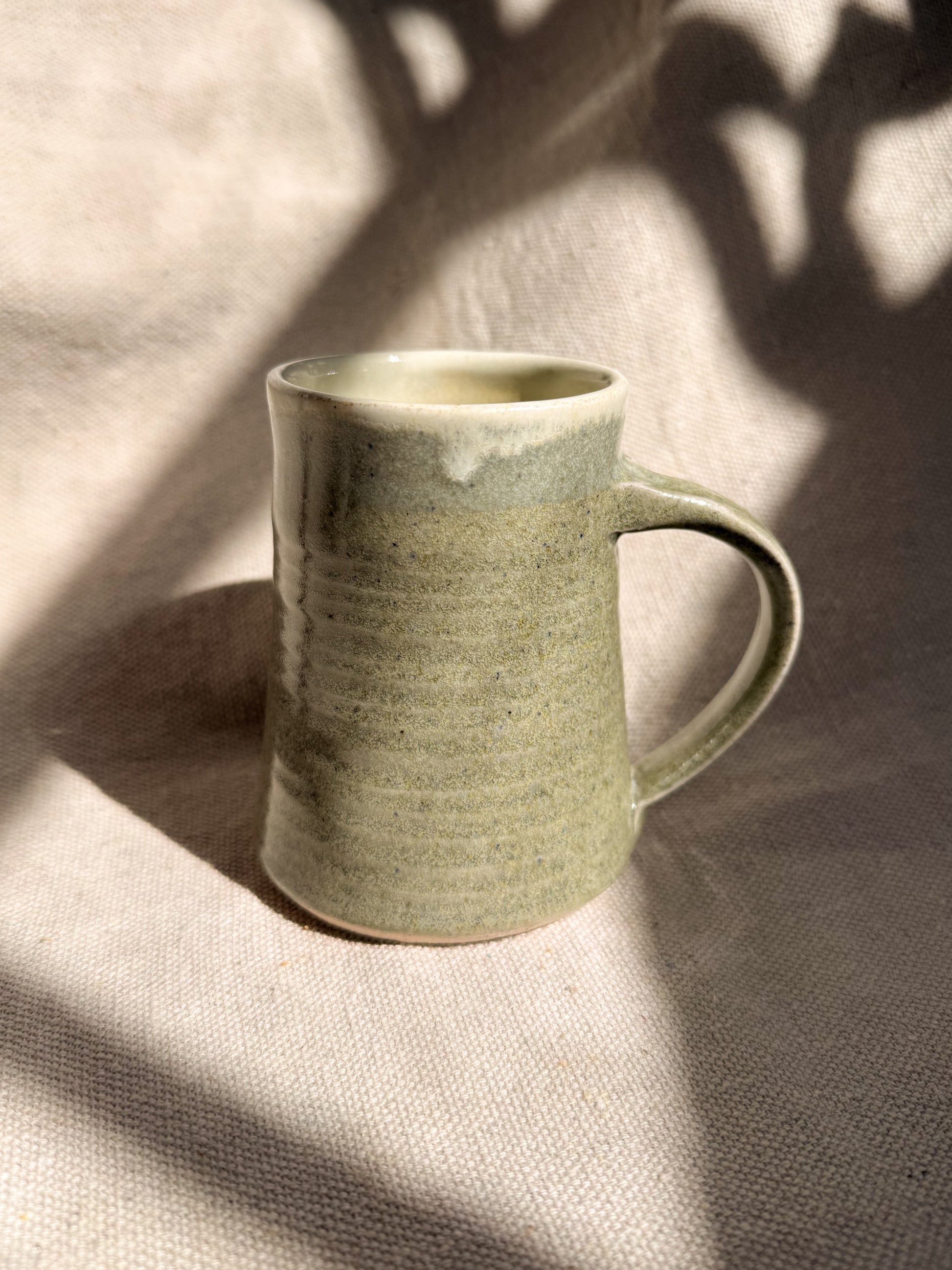 Green ceramic mug on a textured surface with shadows