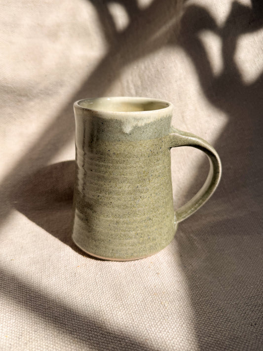 Green ceramic mug on a textured surface with shadows